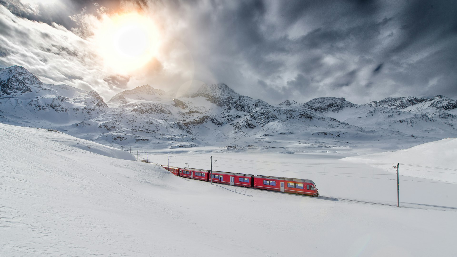 Bernina Express train passing through a snow-covered mountain range.