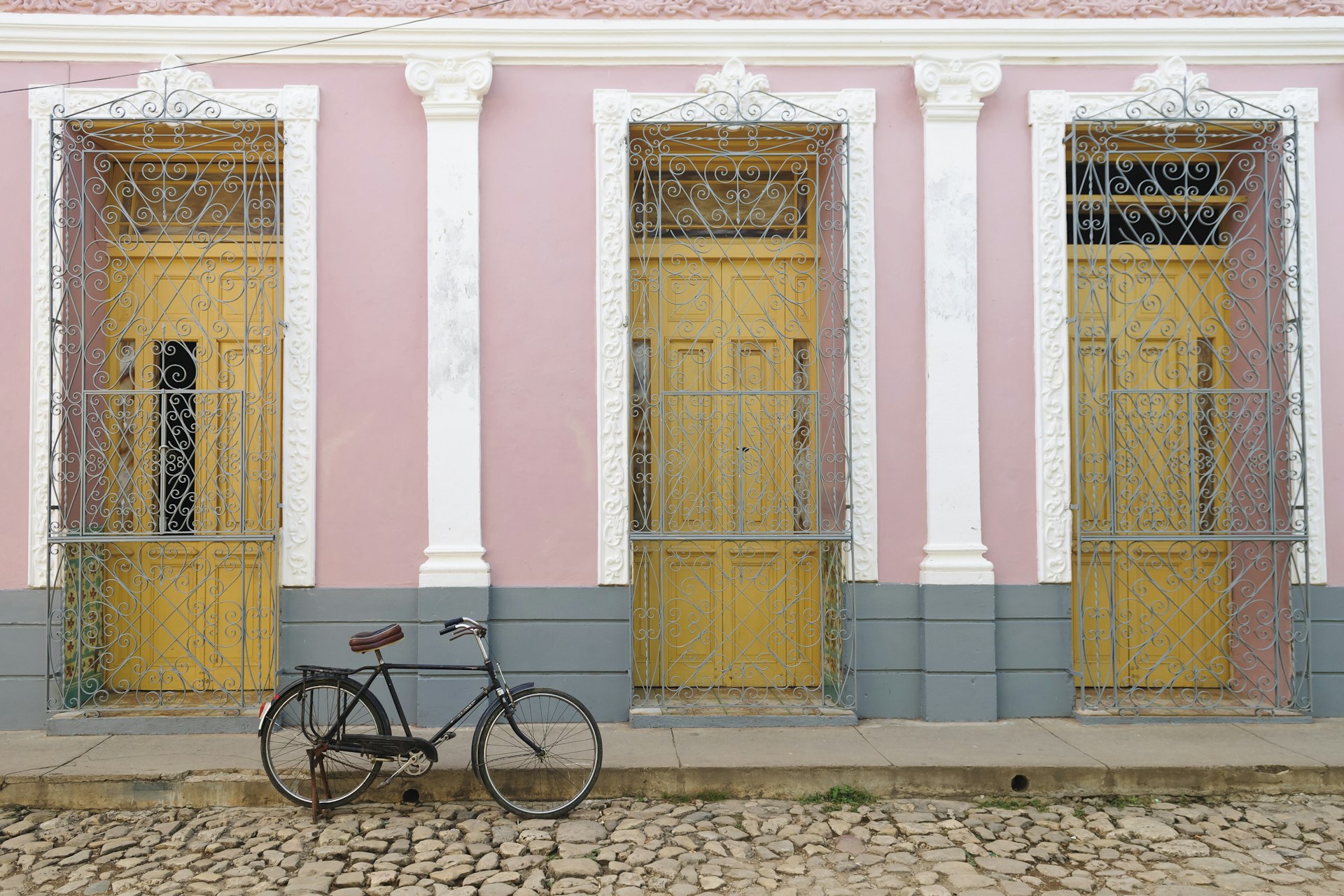 Typical pastel-colored house with wooden front doors framed by plaster motifs and wrought-iron ornamental grills, Trinidad.