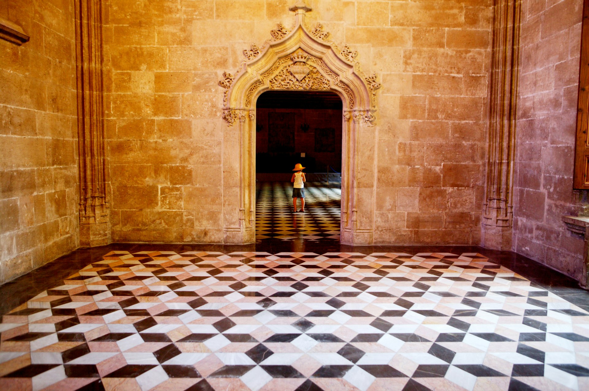 A small child stands in the doorway of a Gothic building with a black-and-white tiled floor