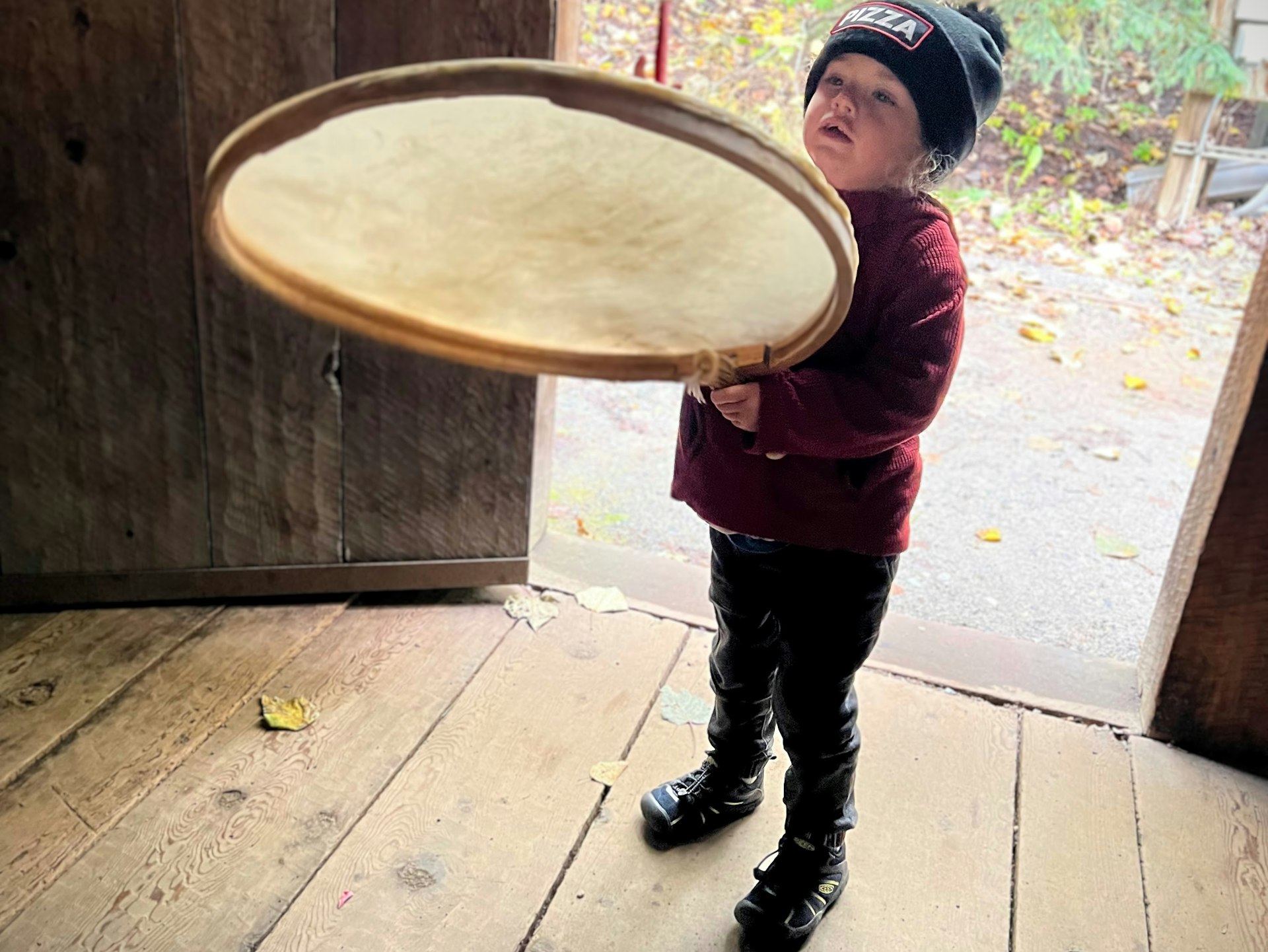 A small white boy in a red top plays a giant drum at the Alaska Native Heritage Center in Anchorage