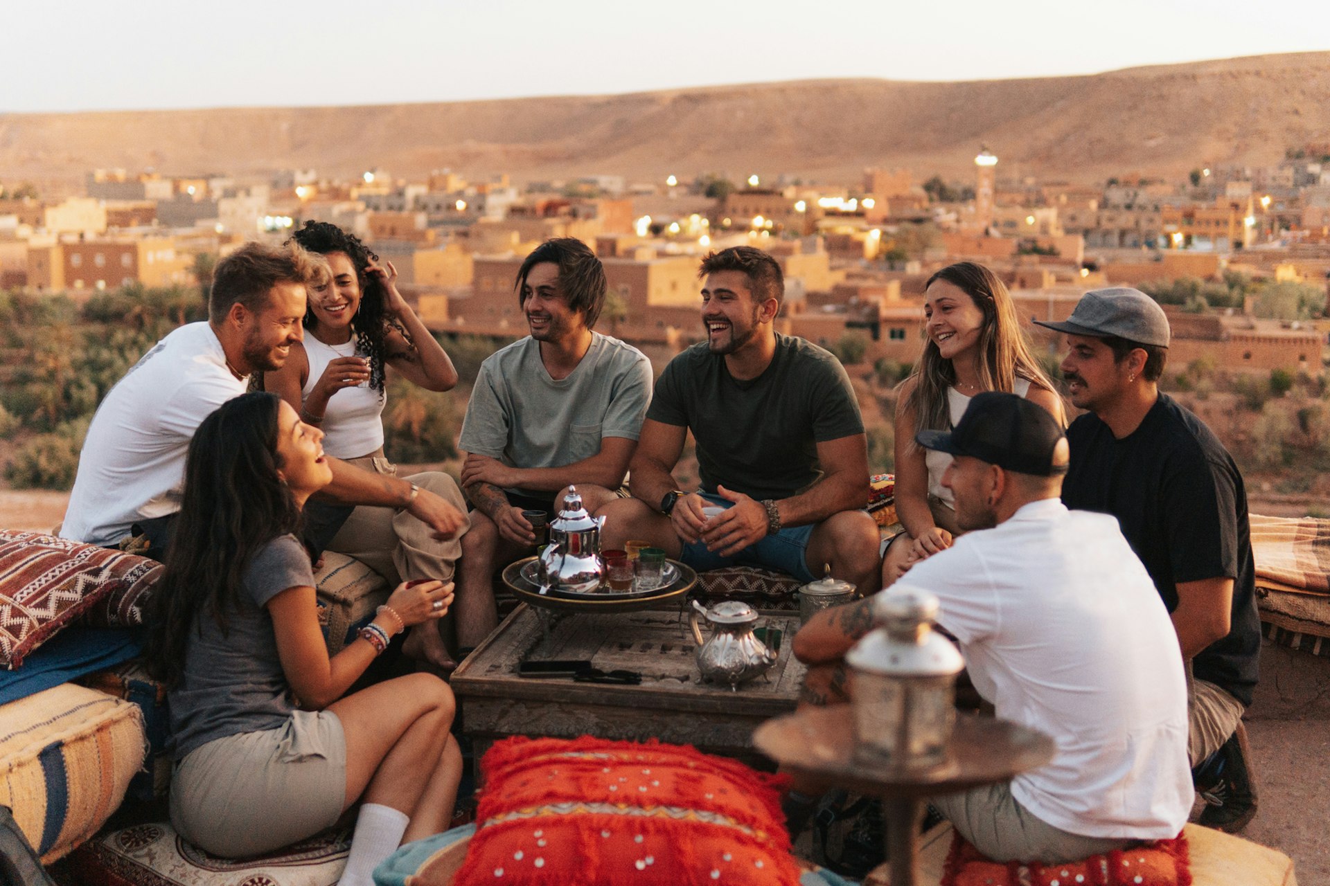 A group of friends smiling and laughing while enjoying tea at a Moroccan teahouse.