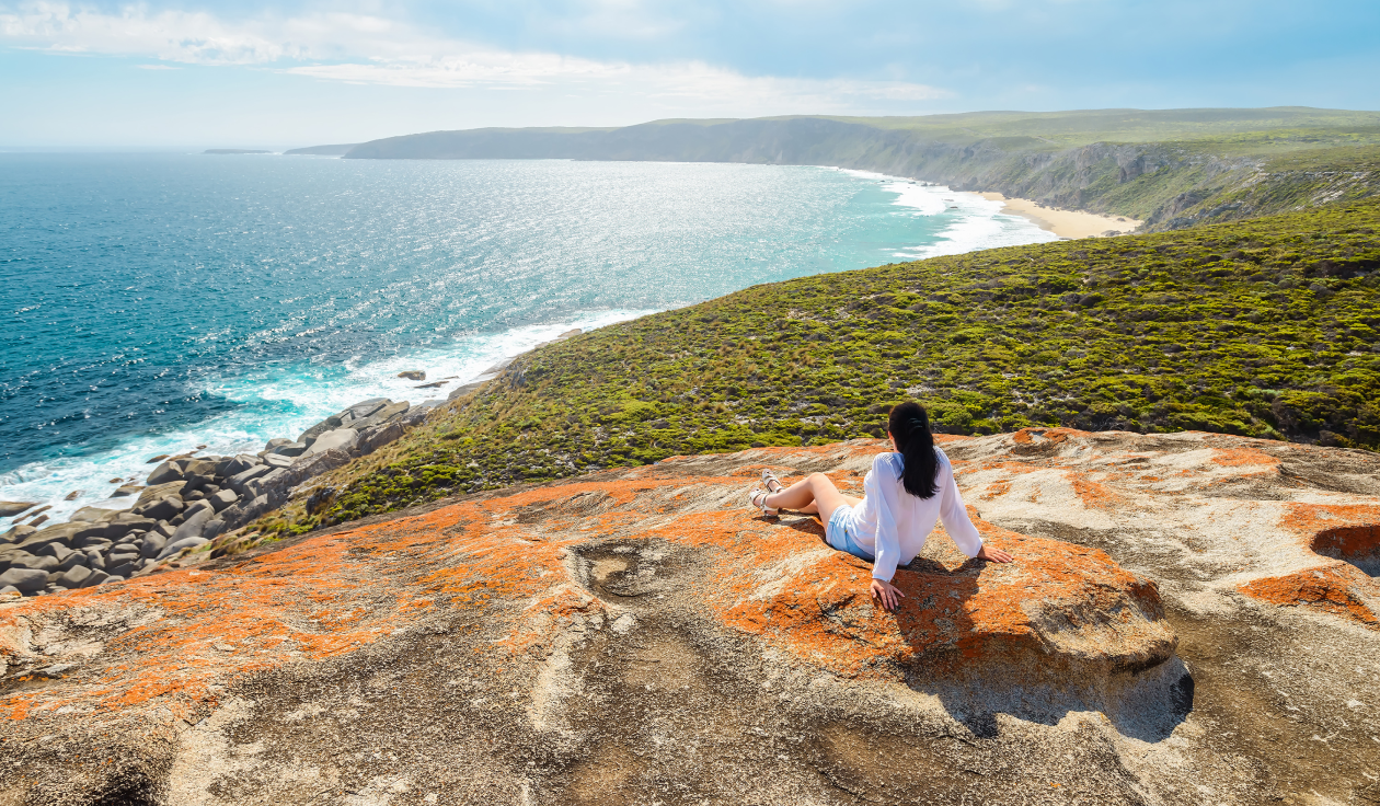 Woman sitting on rocky hill overlooking the ocean