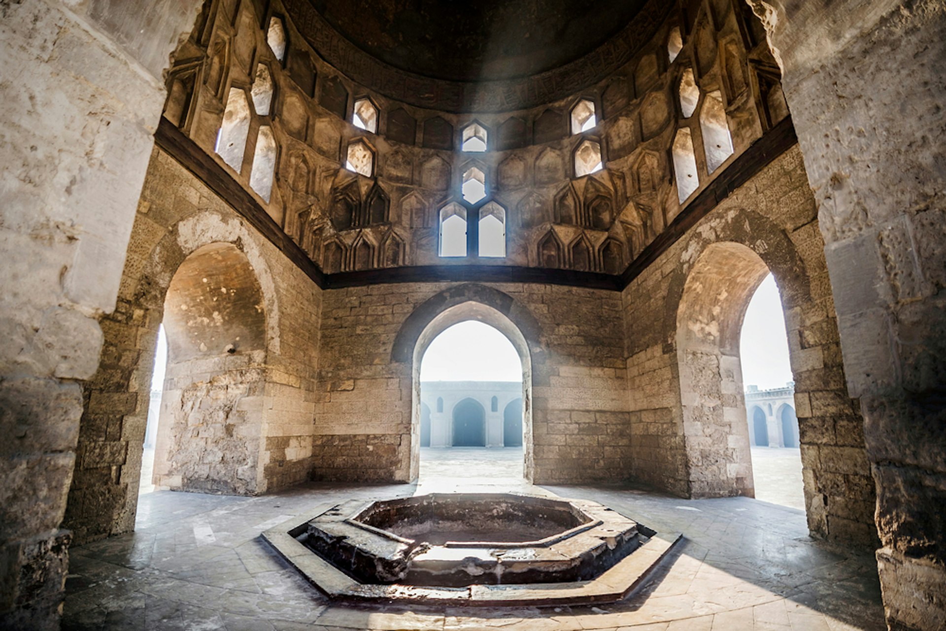 Light flows through windows into a hexagonal building within a mosque complex