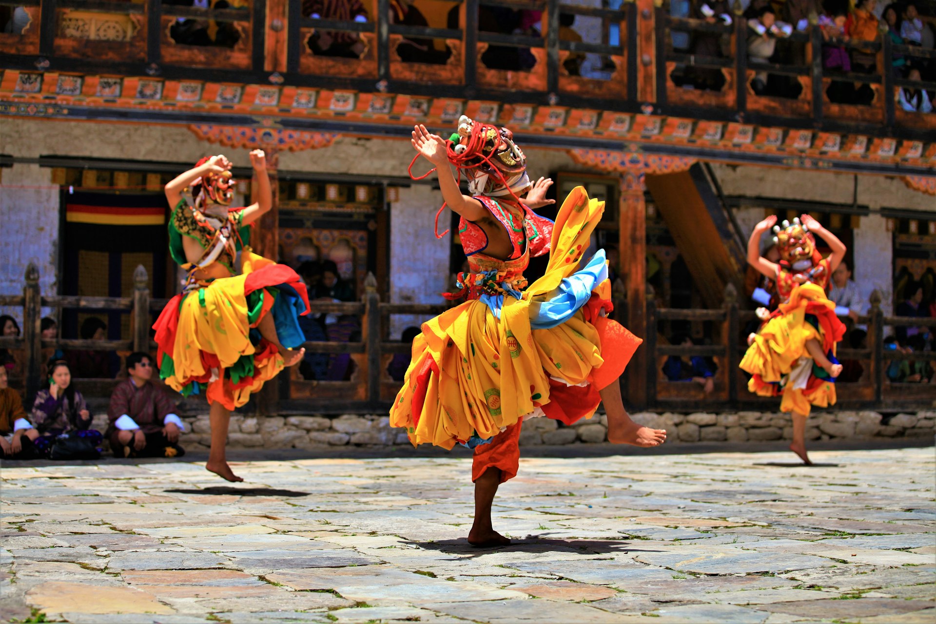 People dancing in colorful masks in a courtyard full of spectators