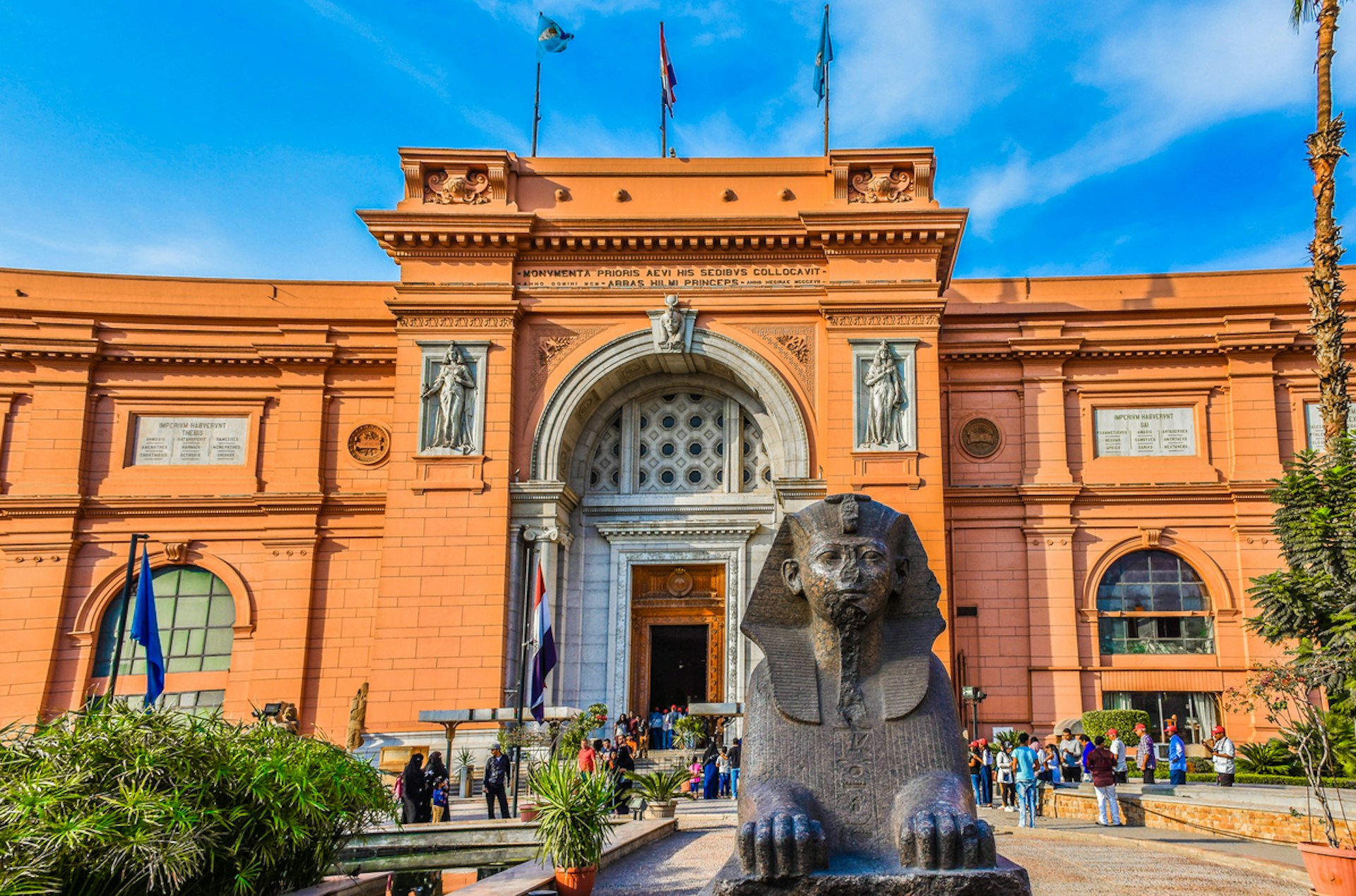 A sphinx outside a salmon-pink historic building in a city square