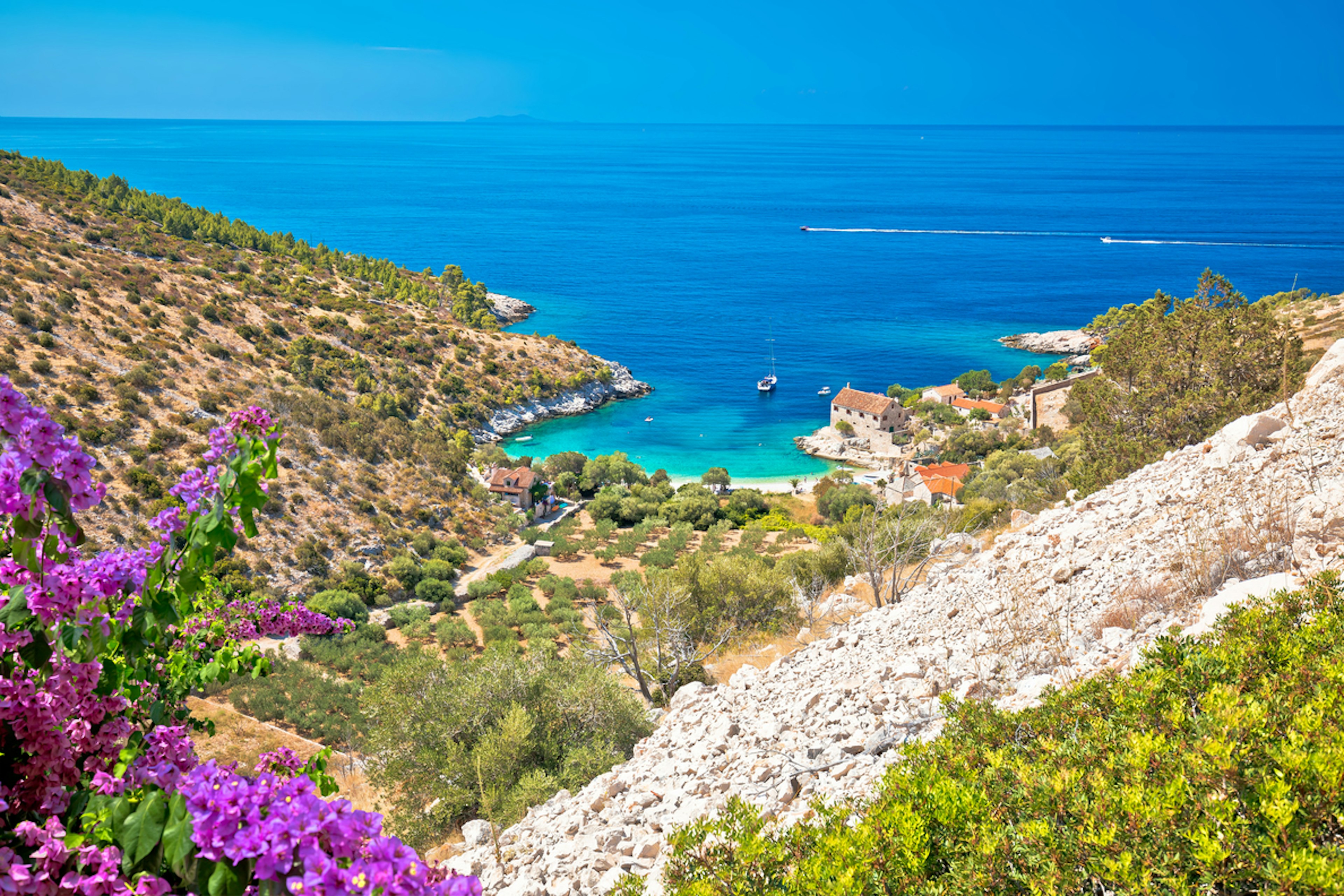 A small beach at the foot of a large hill backed by turquoise ocean