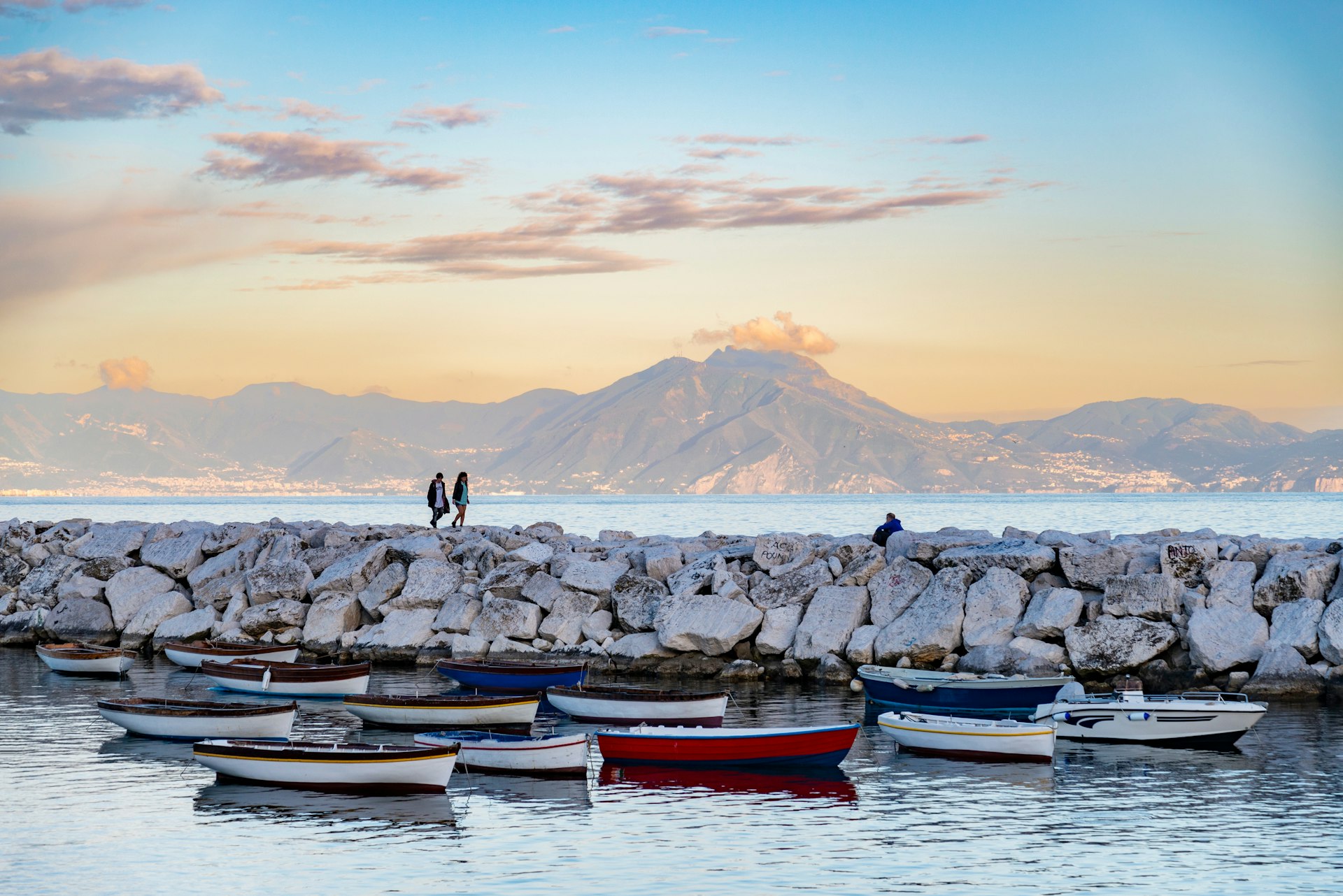 Two people walk along the Napoli waterfront at dusk