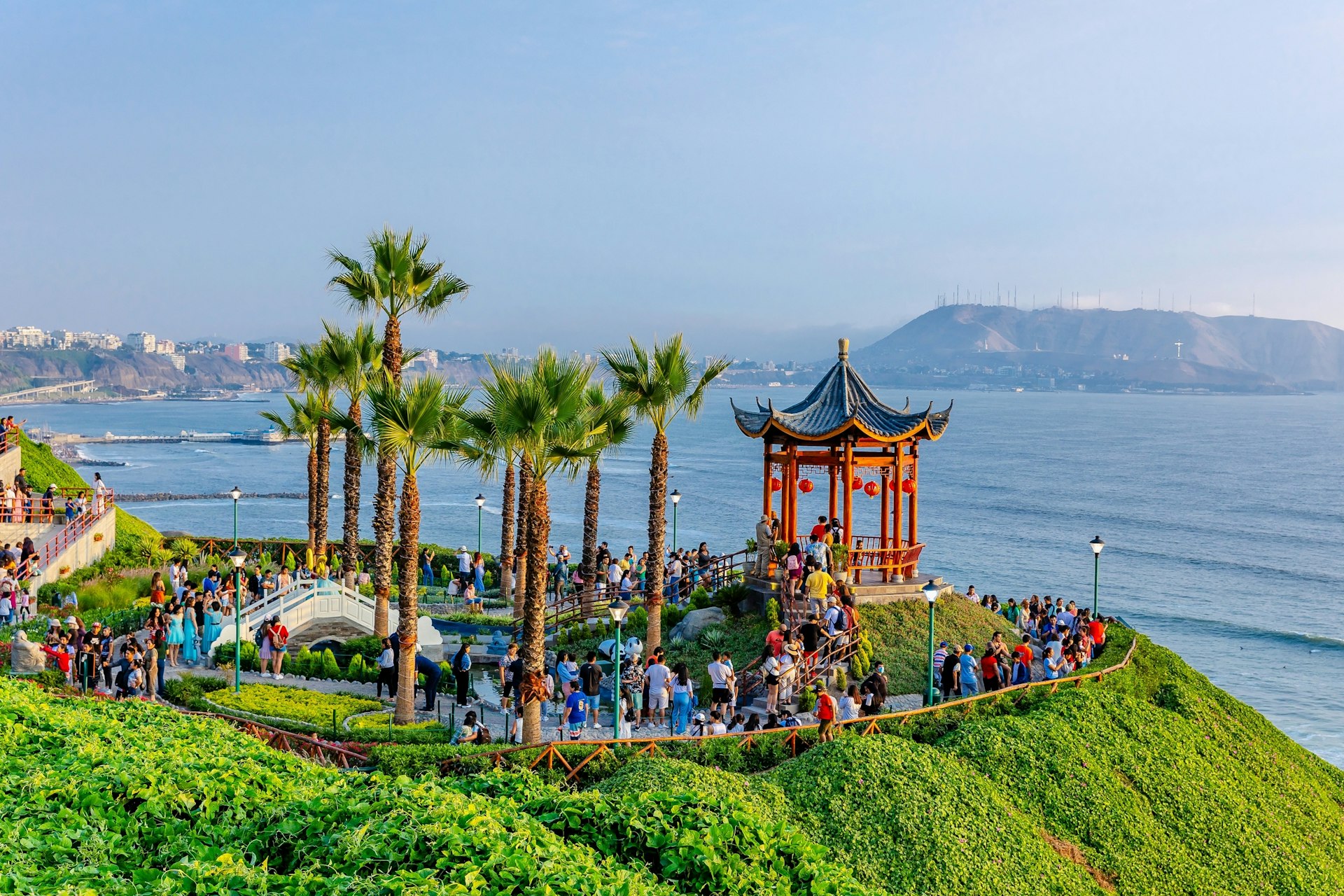 A red Chinese-style pagoda sits on a bluff surrounded by parkland with the sea below it