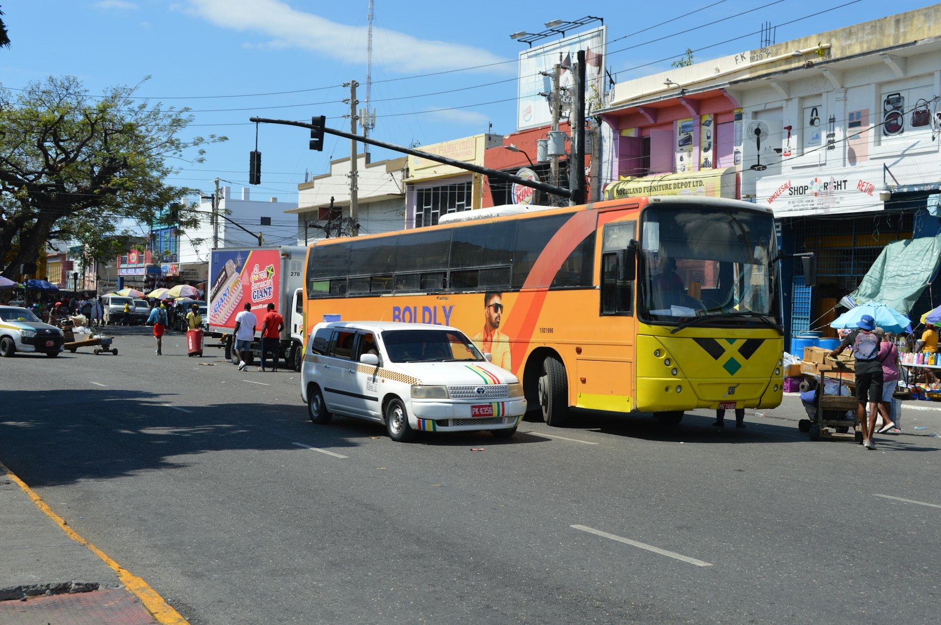 A bright yellow bus, a taxi and commuters on a street in downtown Kingston