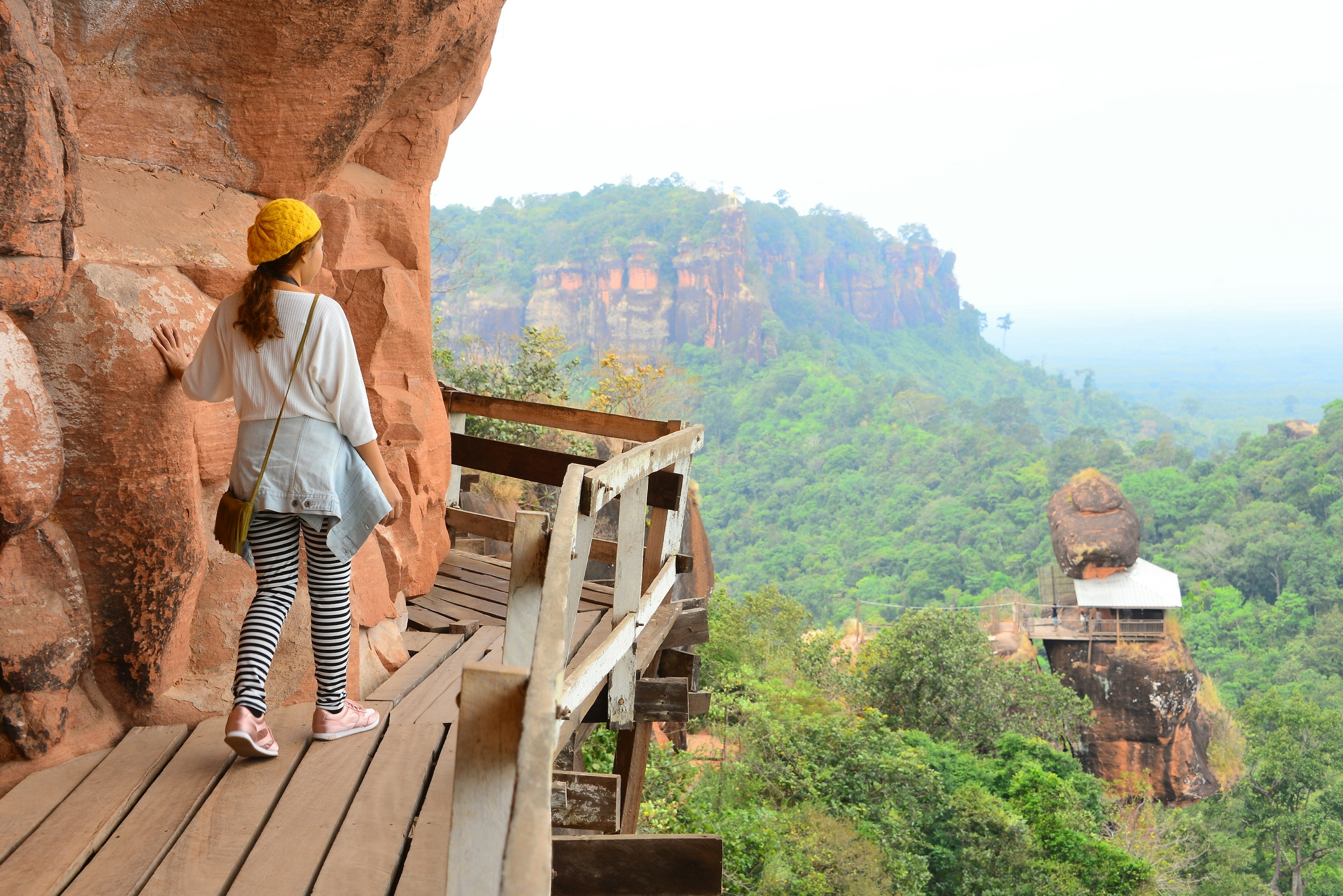 A hiker takes some tentative steps out onto a suspended wooden walkway that clings to the side of a mountain