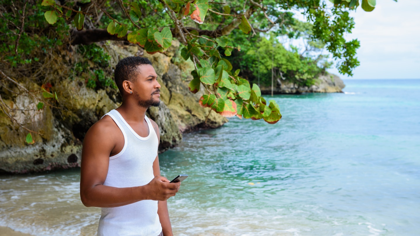 Man standing on a beach with phone in his hand looking out to the deep blue ocean; island destinations