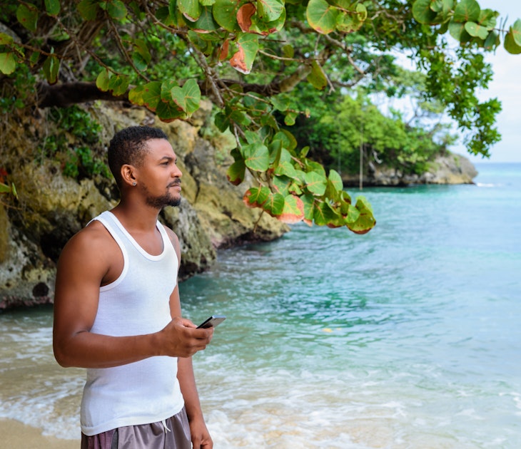 Man standing on a beach with phone in his hand looking out to the deep blue ocean; island destinations