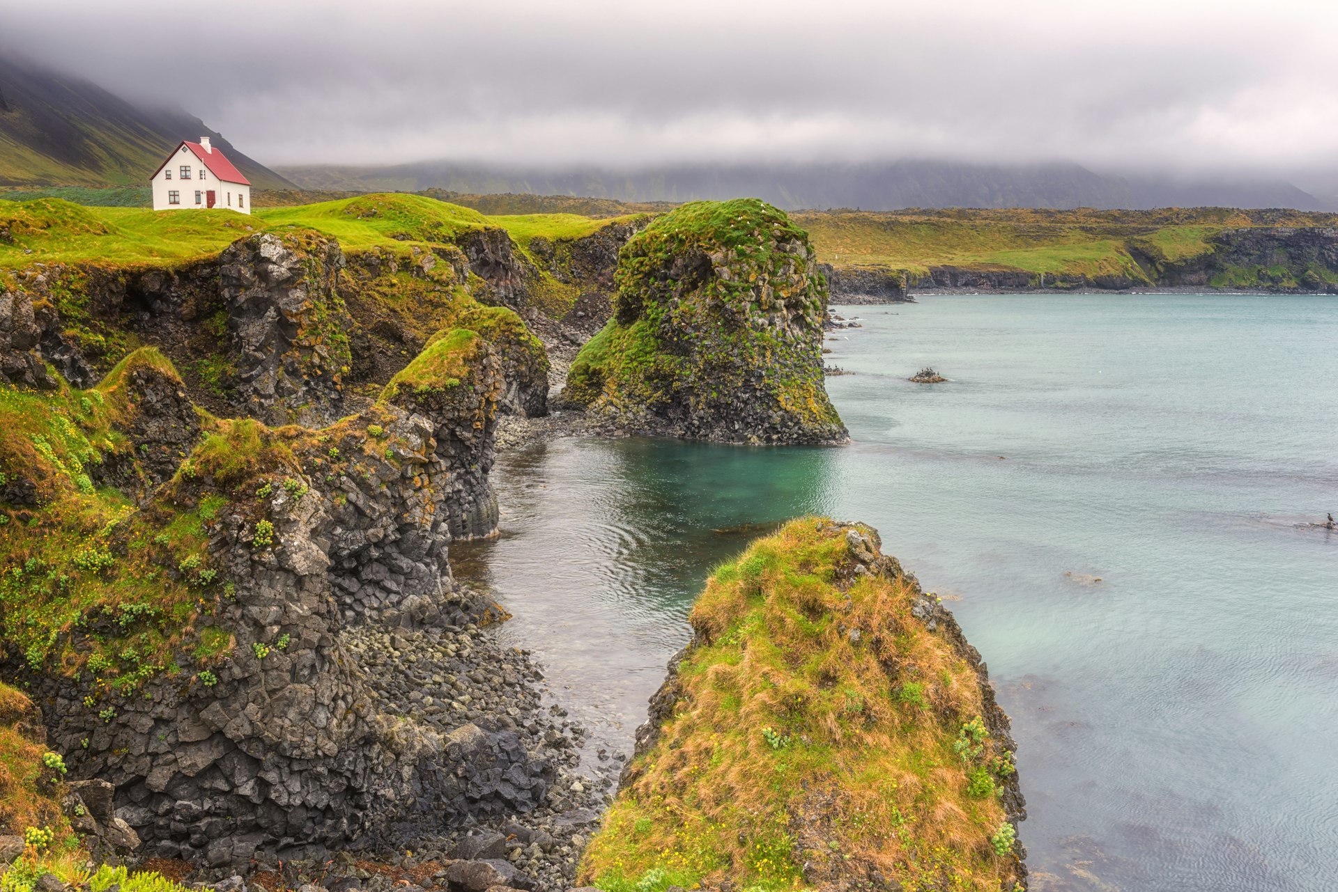 A white house by the volcanic coastal cliffs of Arnarstapi in Iceland