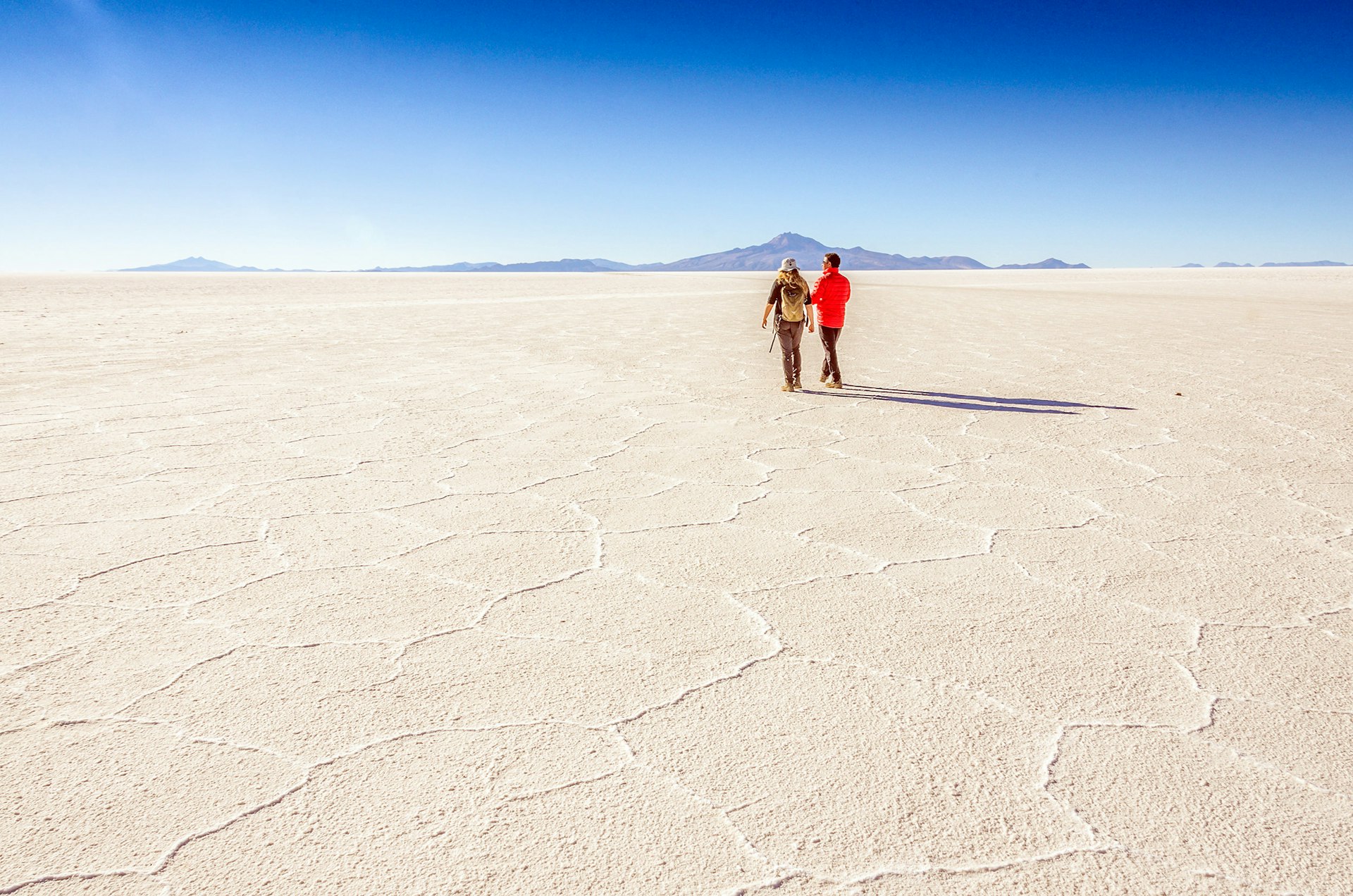 Pair of tourists walking on the vast white salt flats of Salar de Uyuni.