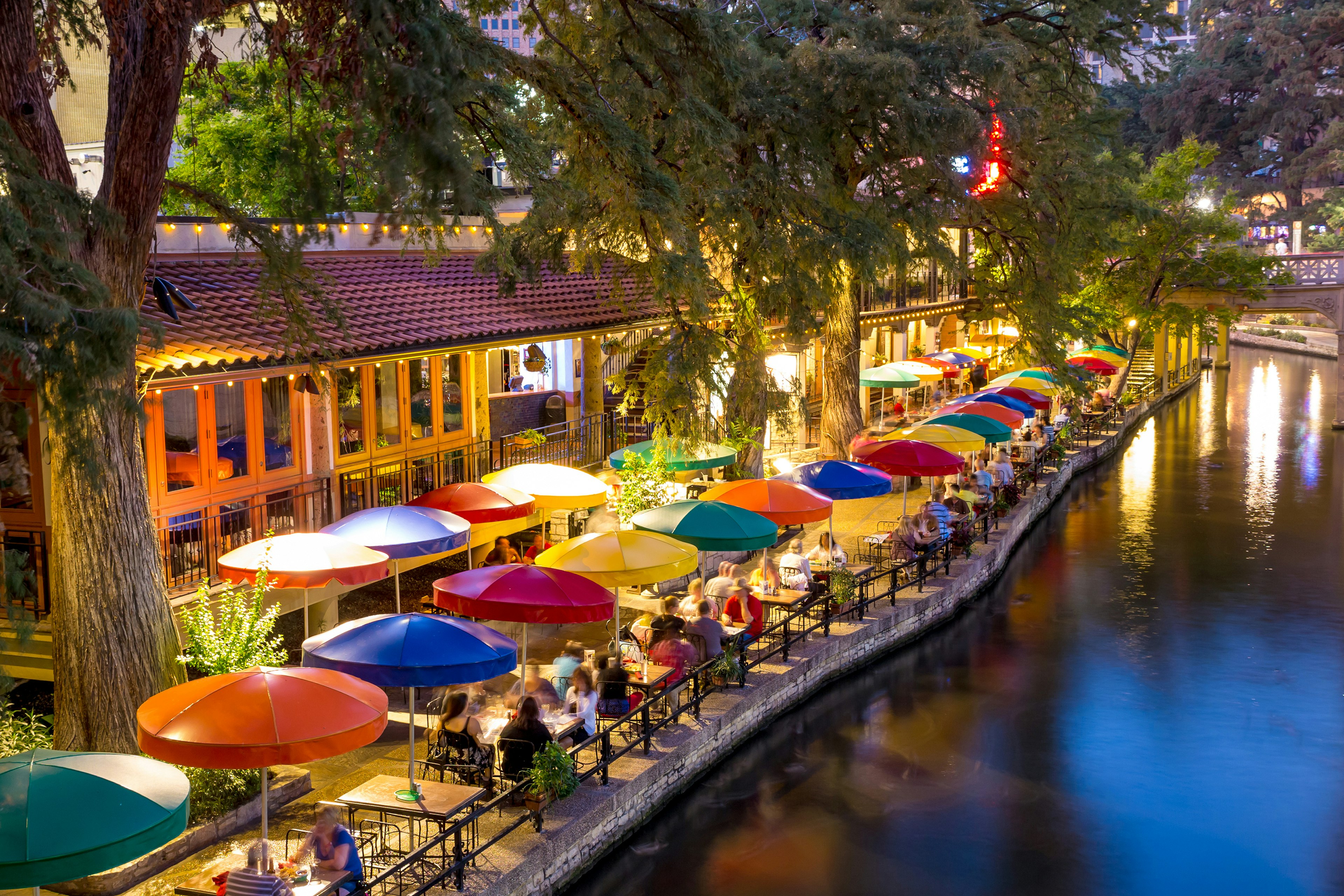 Colorful umbrellas line a waterway with people dining nearby