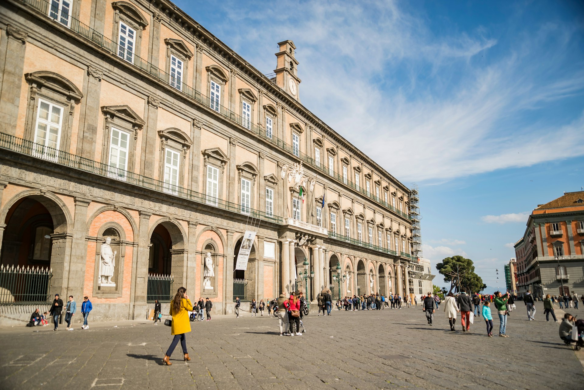 Tourists walk in front of the facade of the historical Royal Palace in Naples