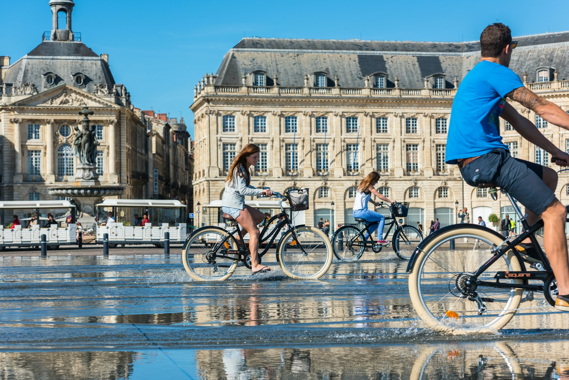 People riding bicycles in the mirror fountain in front of the Palais de la Bourse in Bordeaux, France