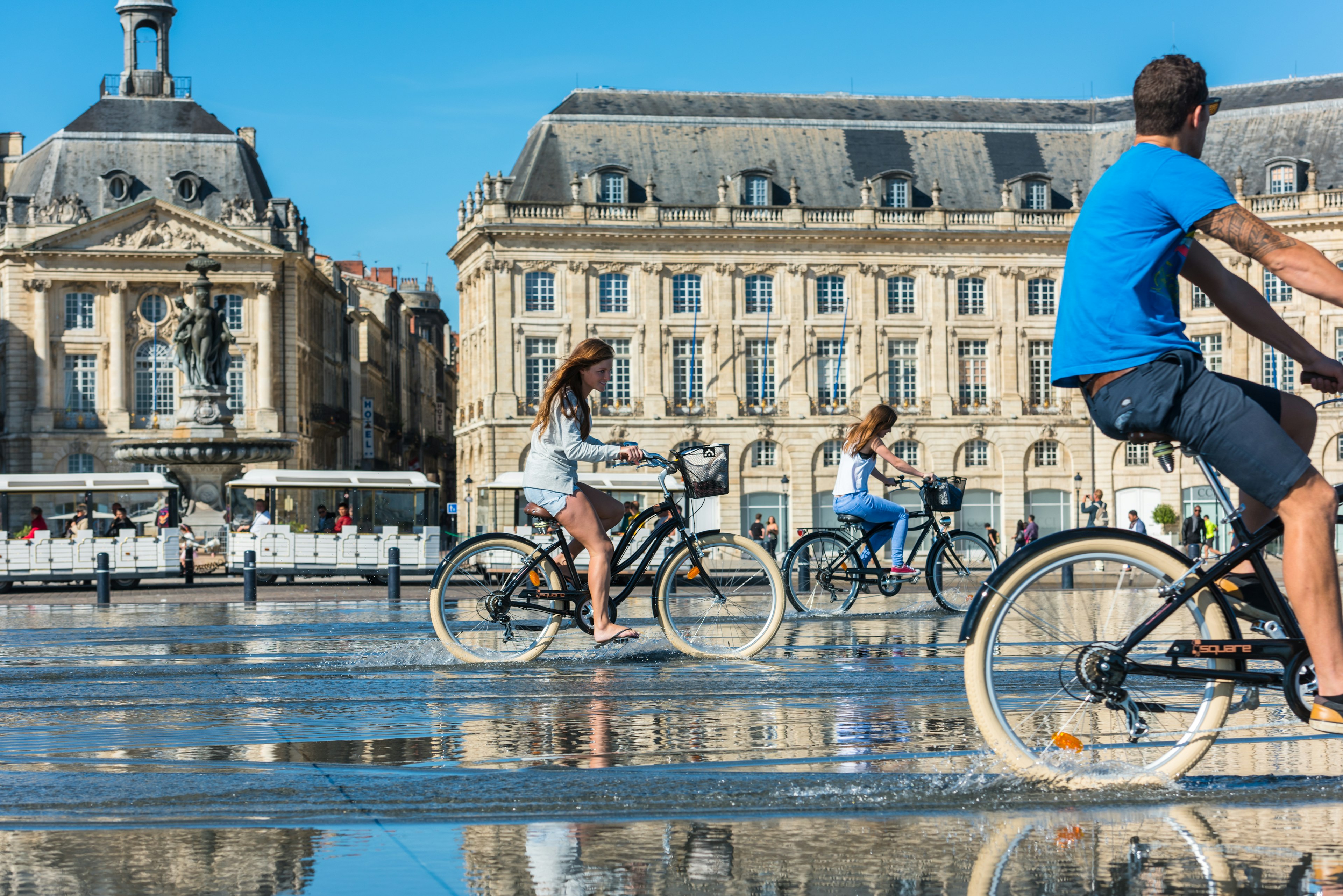 People riding bicycles in the mirror fountain in front of Place de la Bourse in Bordeaux, France