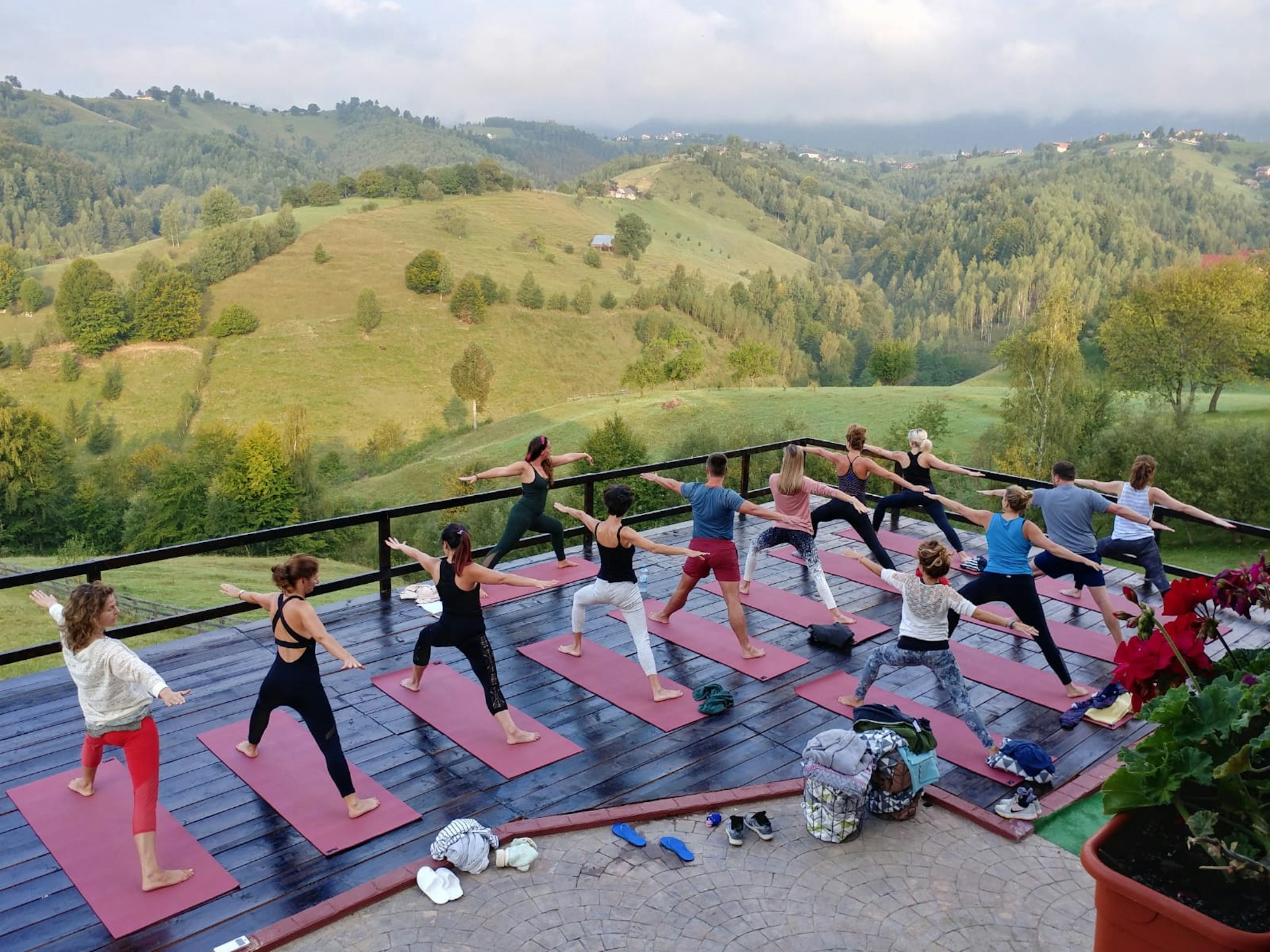 An outdoor yoga class taking place on a terrace overlooking a scenic landscape with rolling hills and trees, with the participants on yoga mats in various poses