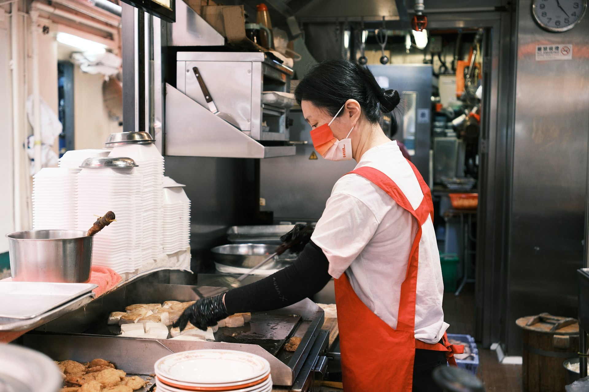 A woman prepares fried tofu on a griddle in an industrial kitchen