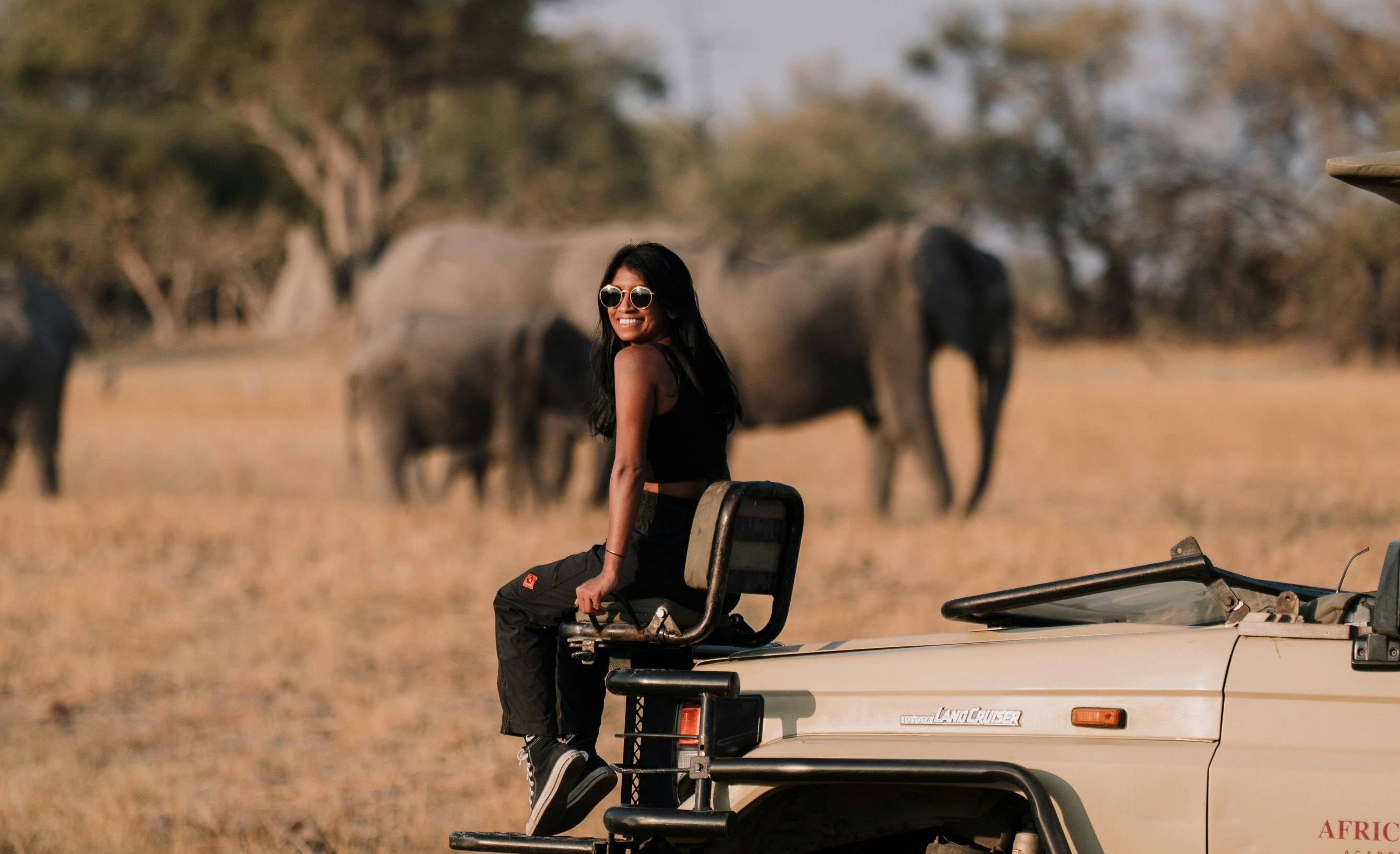 Lonely Planet staff member Deepa Lakshmin sitting on a safari jeep with elephants in Botswana.