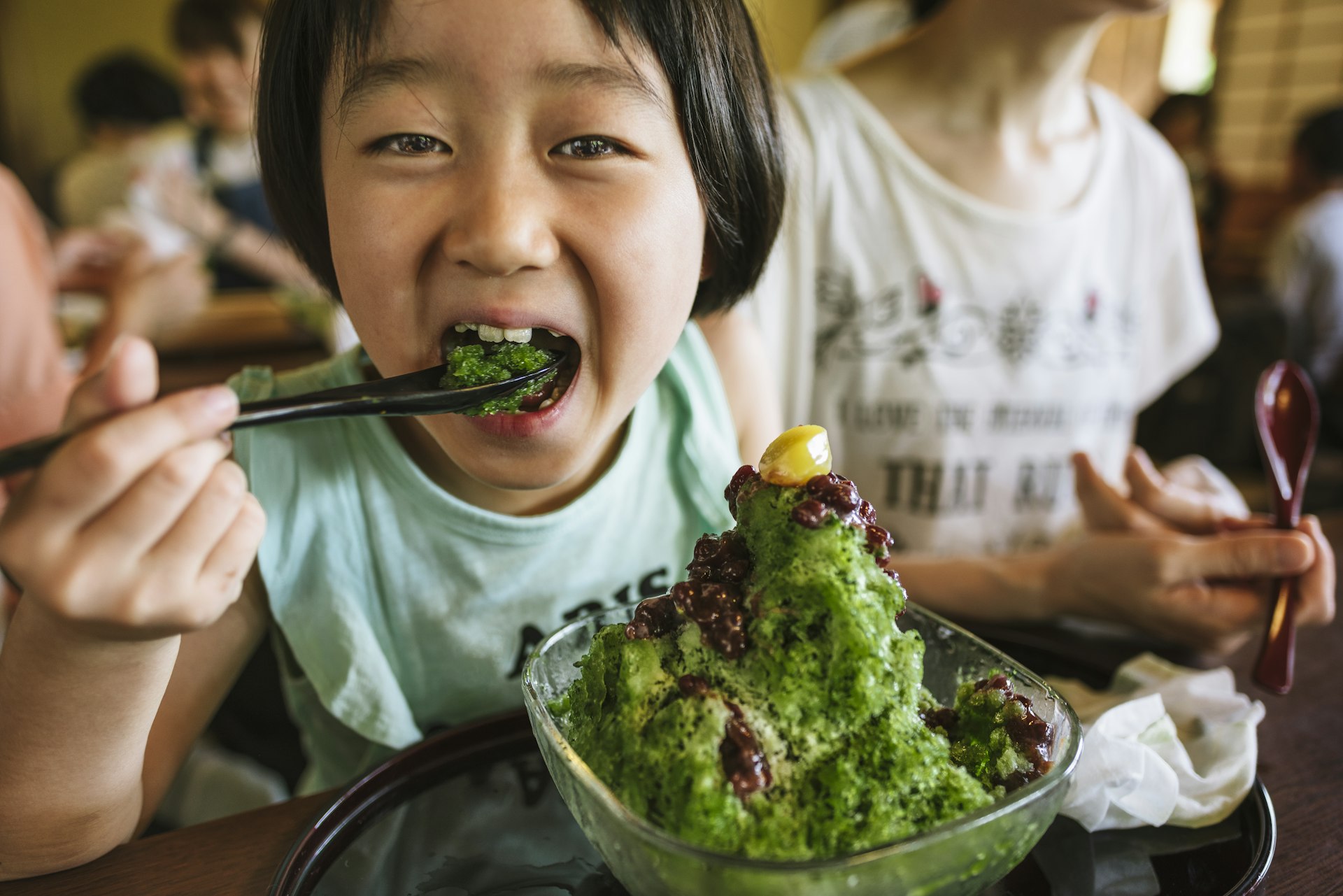 A smiling child takes a bite of green shaved ice in Kyoto