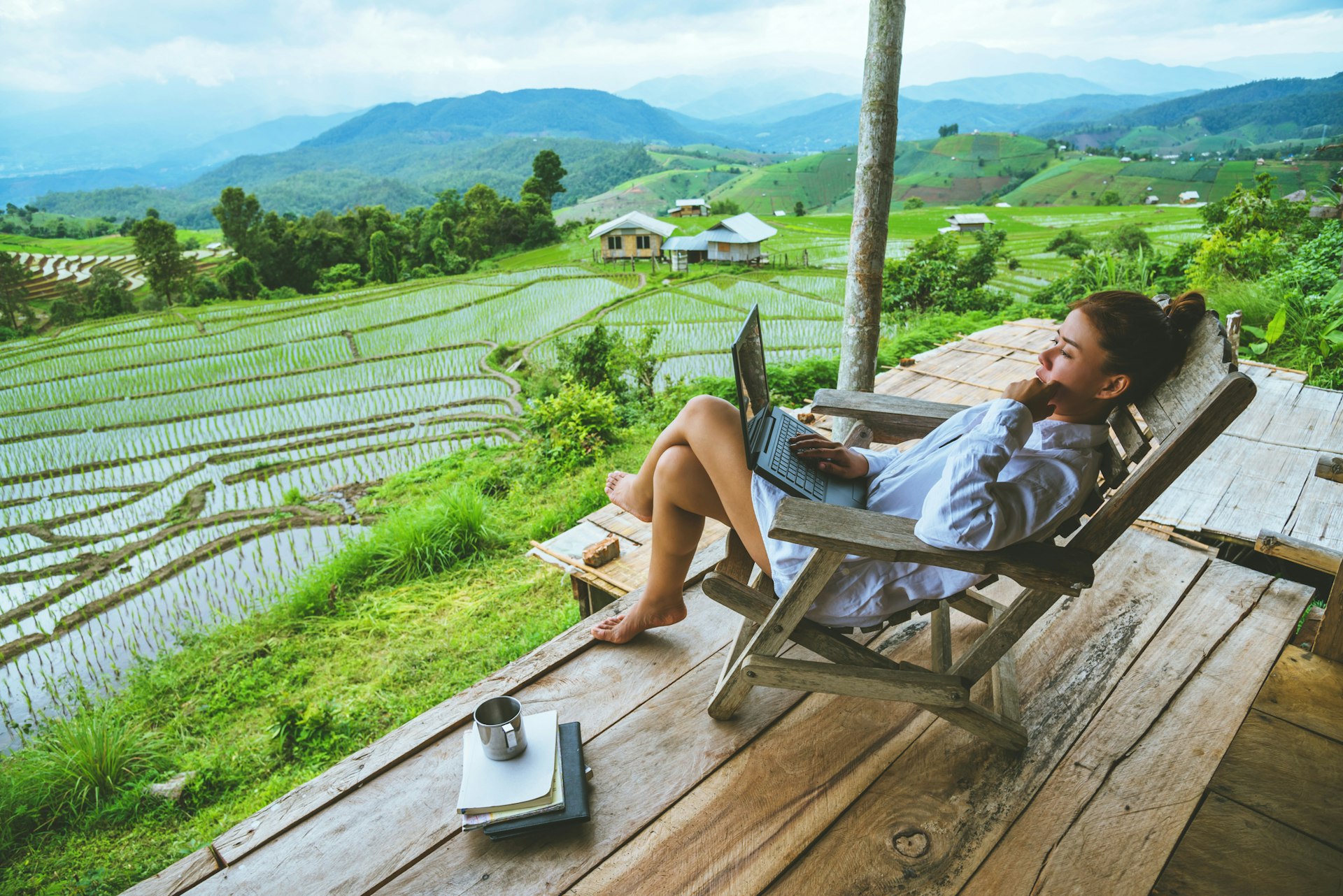 Asian woman travel nature. Travel relax. sit work with a laptop the balcony of the resort. View of the field on the Moutain in summer