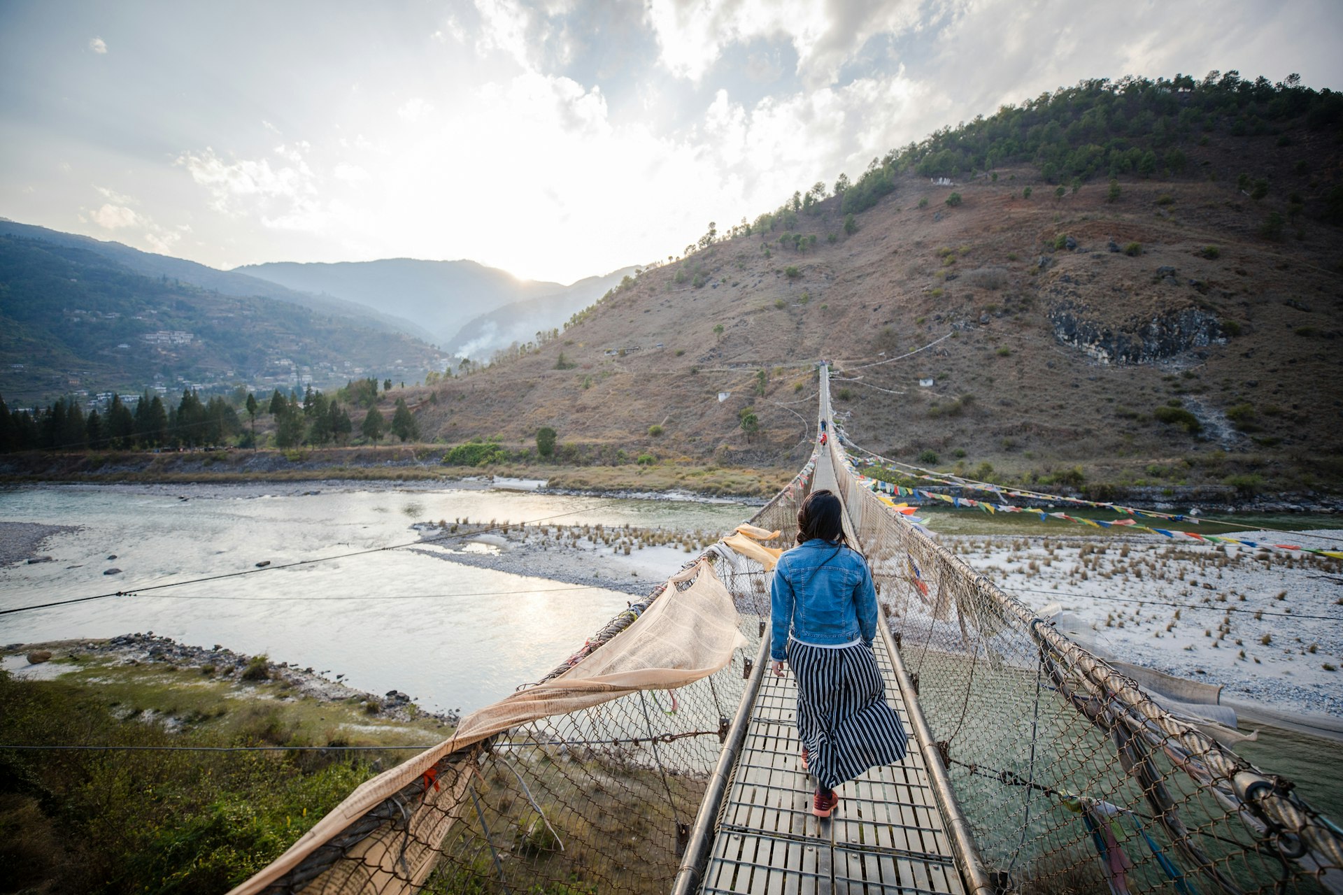 A teen walks along a very long suspension bridge over a river