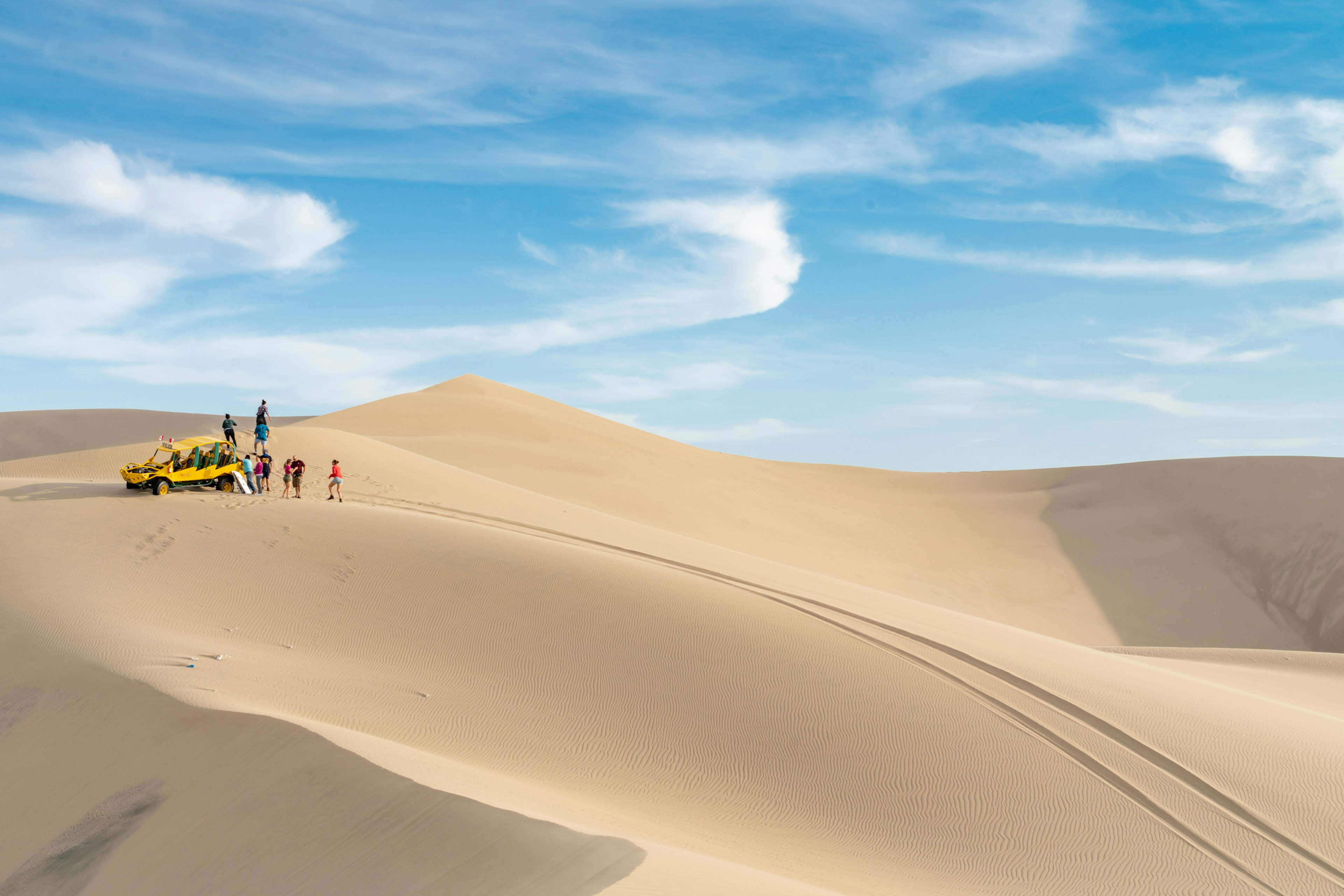 People stand near a dune buggy on vast sand dunes