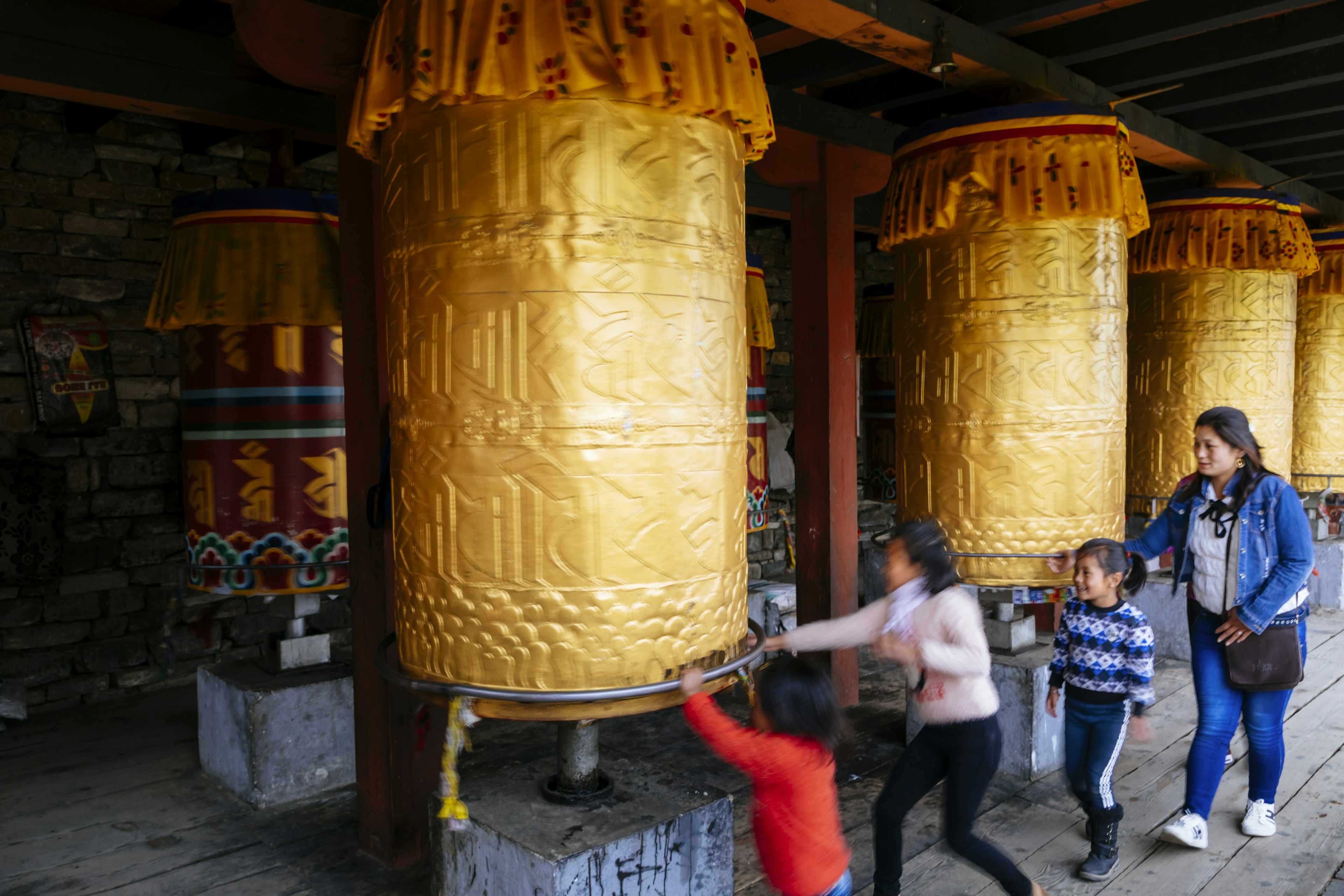 A woman and three young children spinning a prayer wheel in a monastery