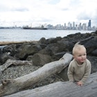 Boy playing on log at Alki Beach with skyline of Seattle in distance.
115700203