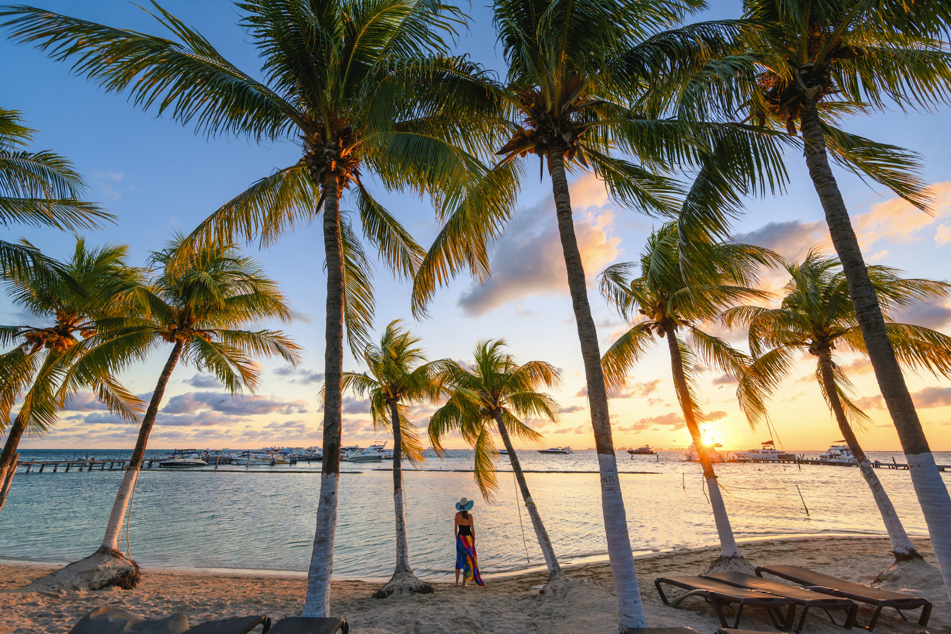 The palm trees and sunsets as seen on Isla Mujeres, Quintana Roo, Mexico with a woman watching the sun go down