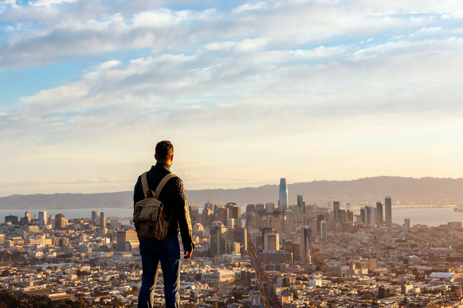 A man with a backpack stands on a high vantage point overlooking a vast cityscape. 