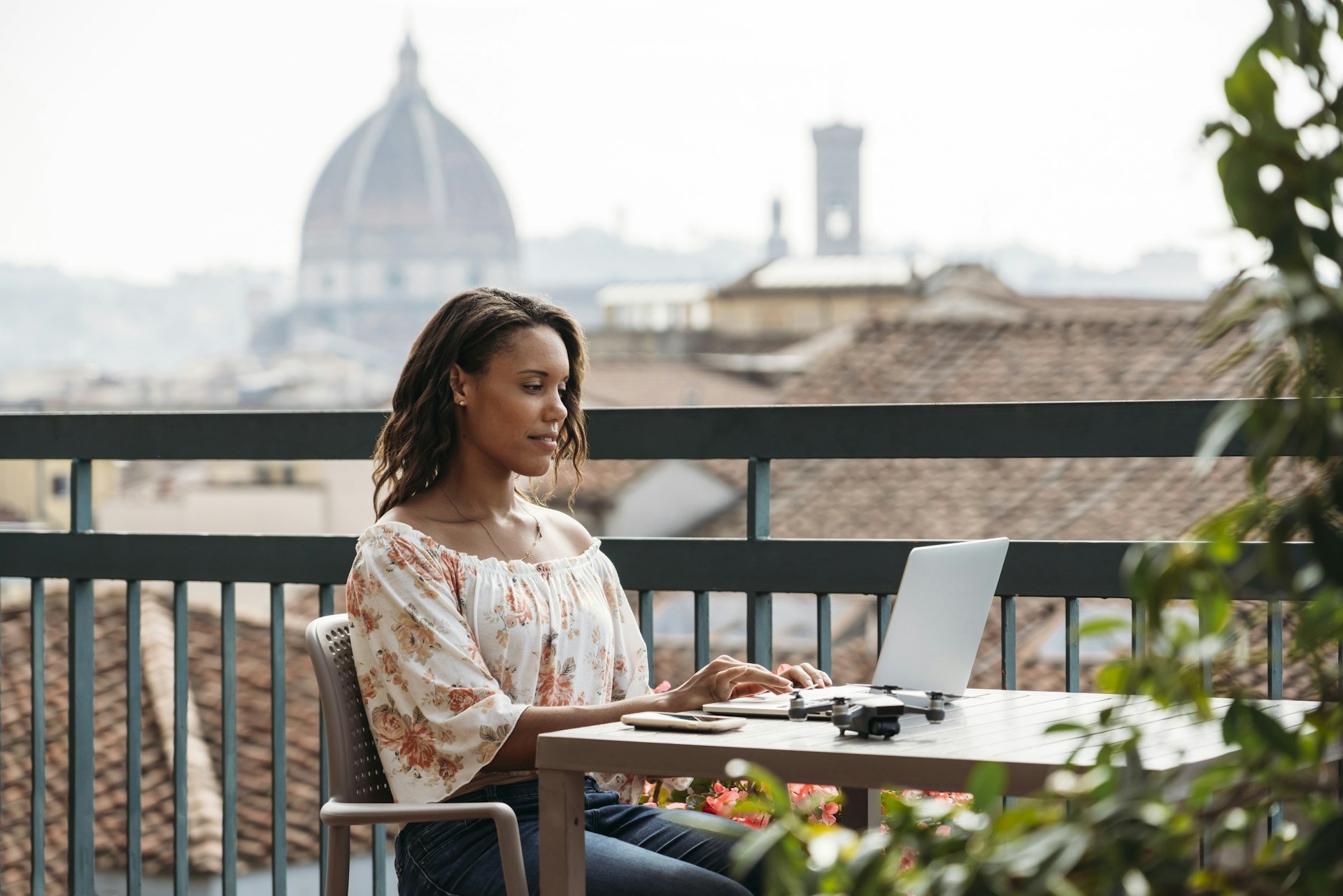 A black woman at a laptop at a cafe in Florence with the city rooftosp in the background