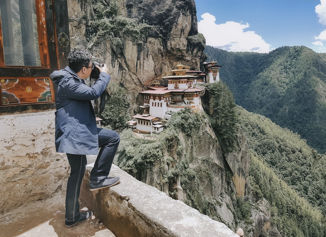 An Asian tourist photographing the Tiger's Nest Monastery in Bhutan