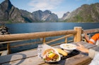 A gourmet meal consisting of a hearty bowl of soup and fresh seafood sandwich is on a dining table overlooking the fjord on a sunny day in Reine, Norway. A finger is touching the soup bowl and just so excited to taste it.
1251407976