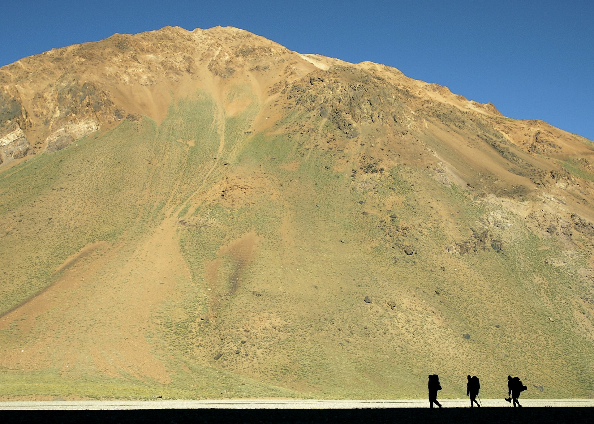 Walkers are silhouetted against the huge mountainside of Cerro Aconcagua, Argentina