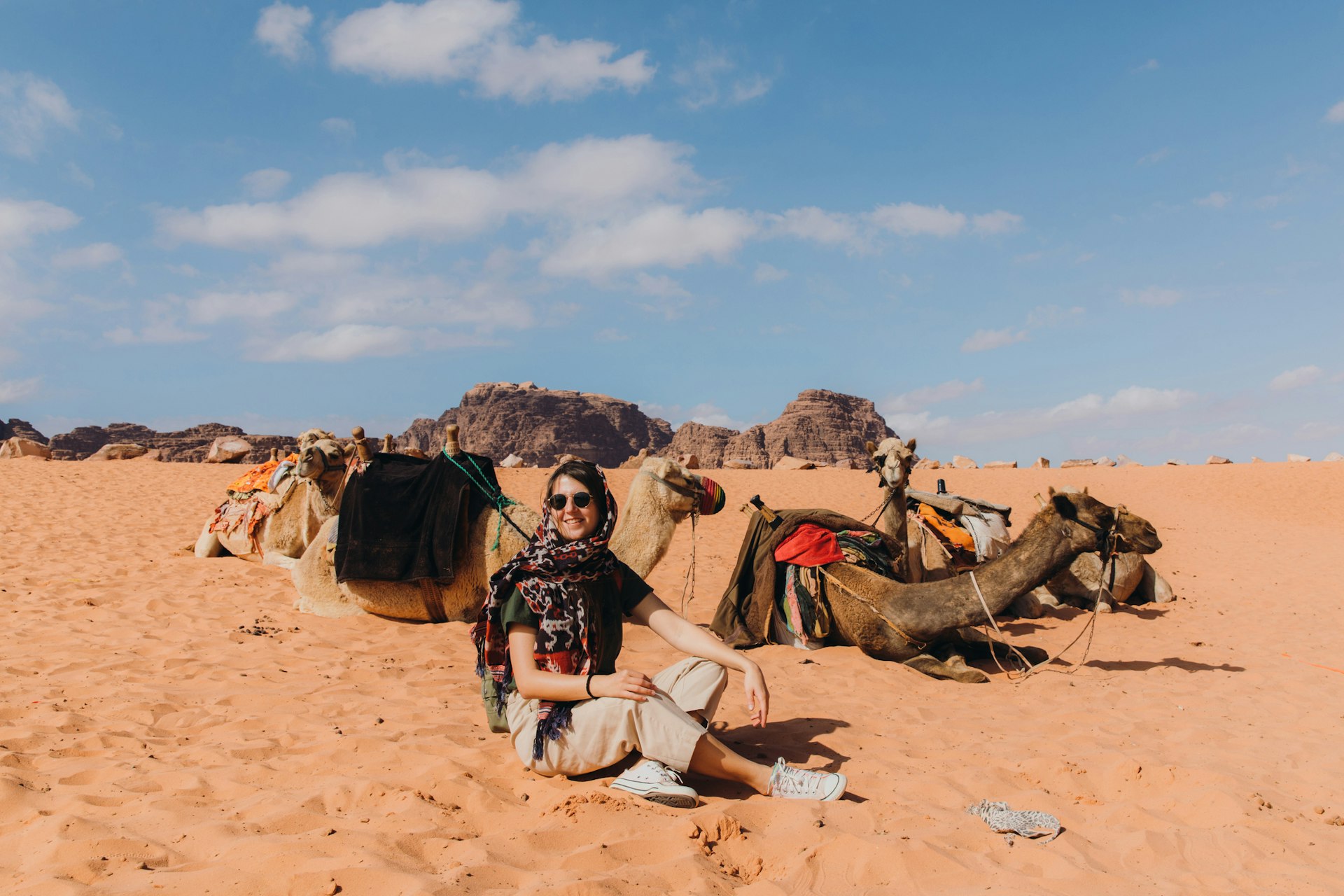 Young woman traveler sitting near group of camels in the Wadi Rum desert