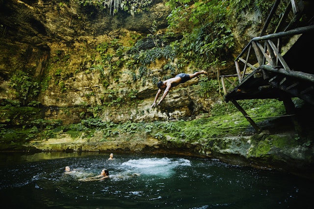 A man dives into a cenote - a sunken water hole - to join friends swimming there