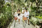 Wide shot of smiling couple walking bikes on pathway in jungle at tropical resort
1366306661
exotic travel
A woman and man walking along a path with bikes in Mexico