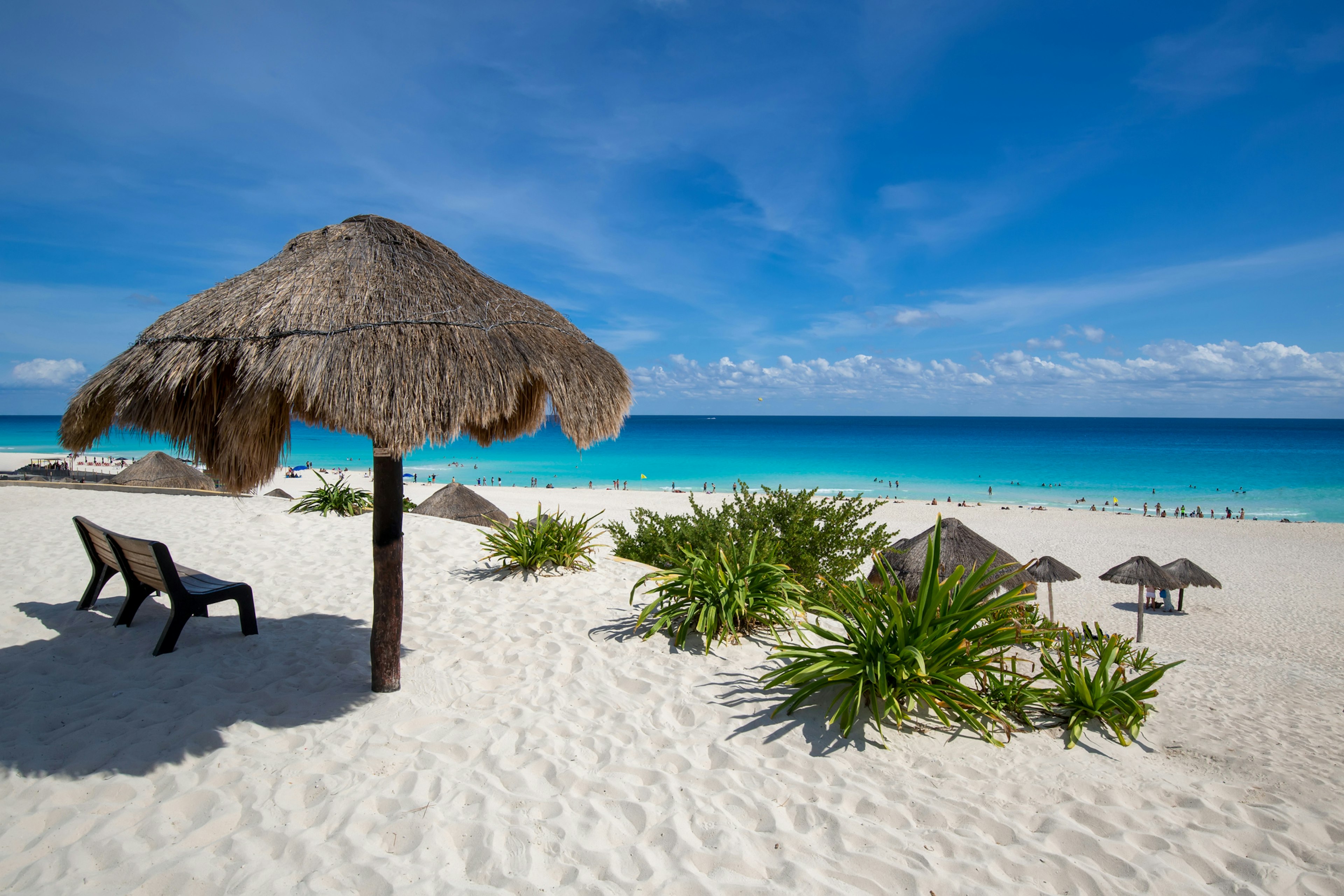 A palm-frond sun shade on a perfect white-sand beach with turquoise ocean lapping at the shore