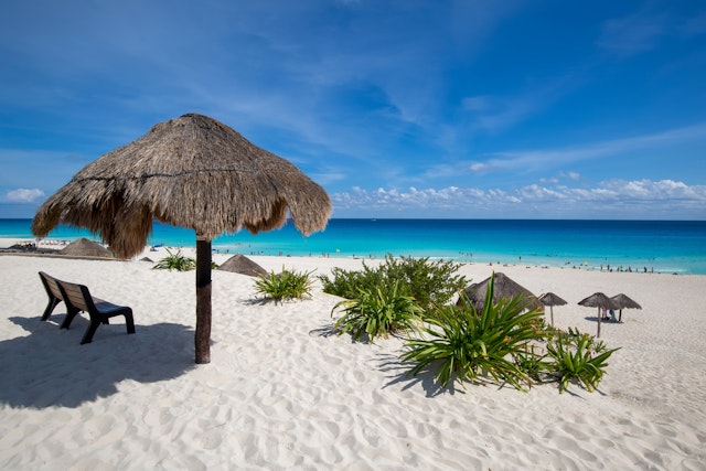 A palm-frond sun shade on a perfect white-sand beach with turquoise ocean lapping at the shore