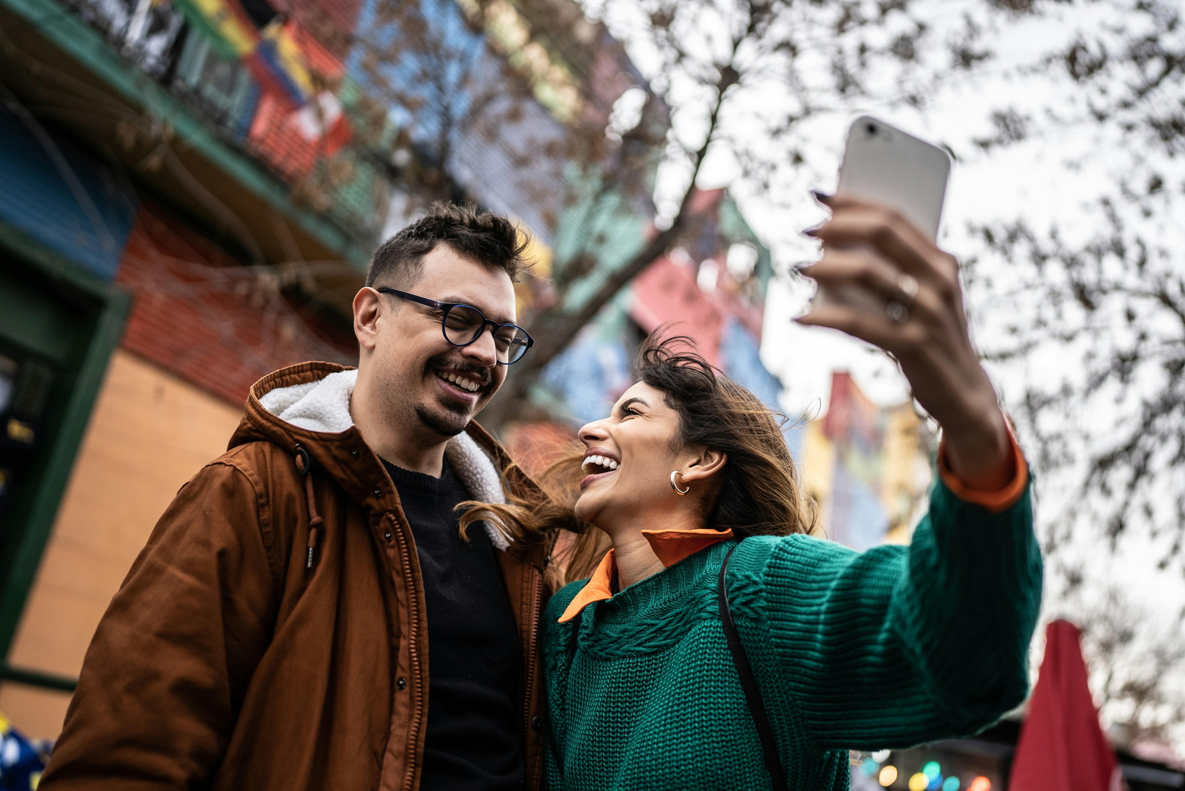 Happy couple taking a selfie outdoors below a tree in Buenos Aires, Argentina with brightly painted houses in the background