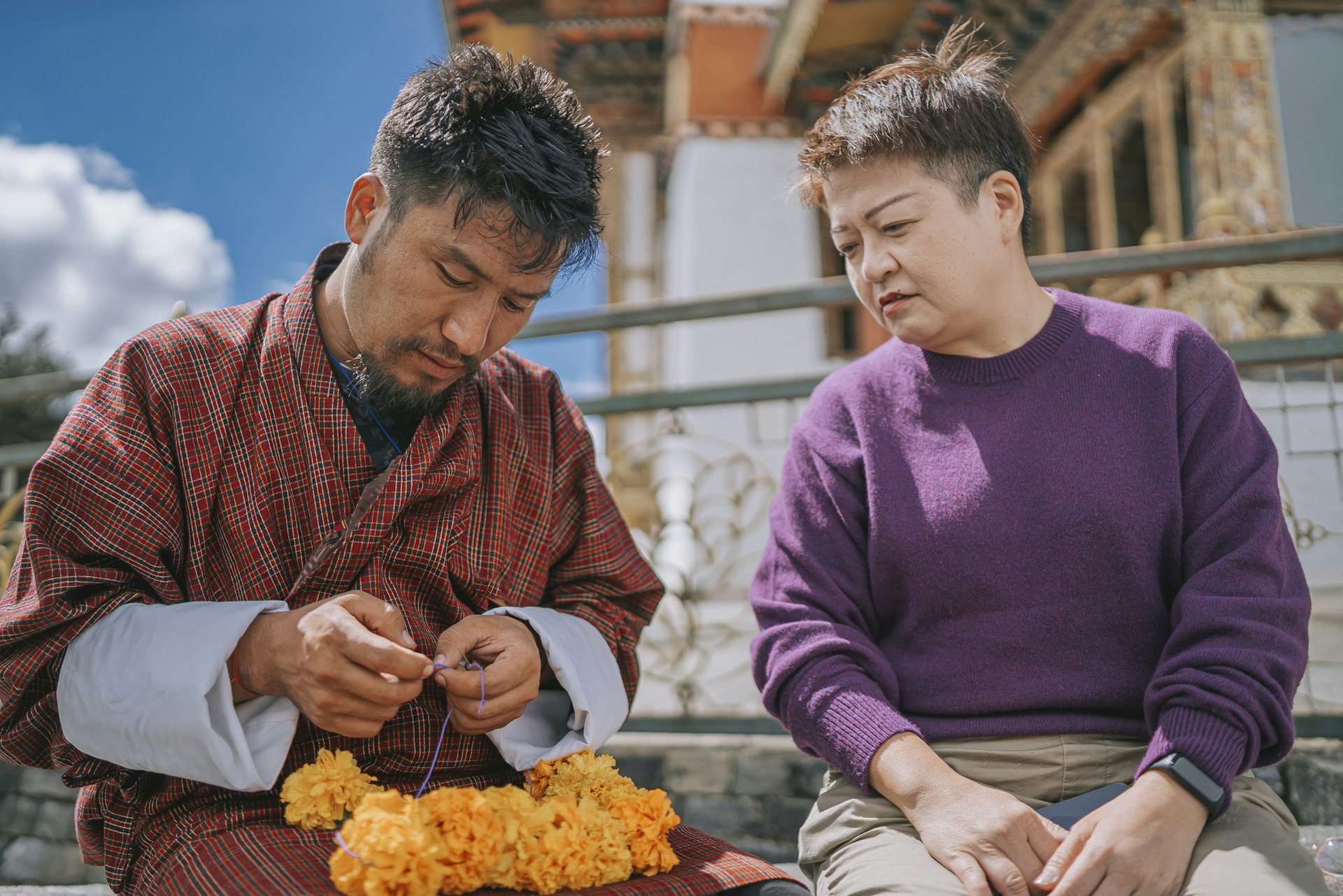 Bhutanese Man shows a Chinese tourist how to make a marigold wreath