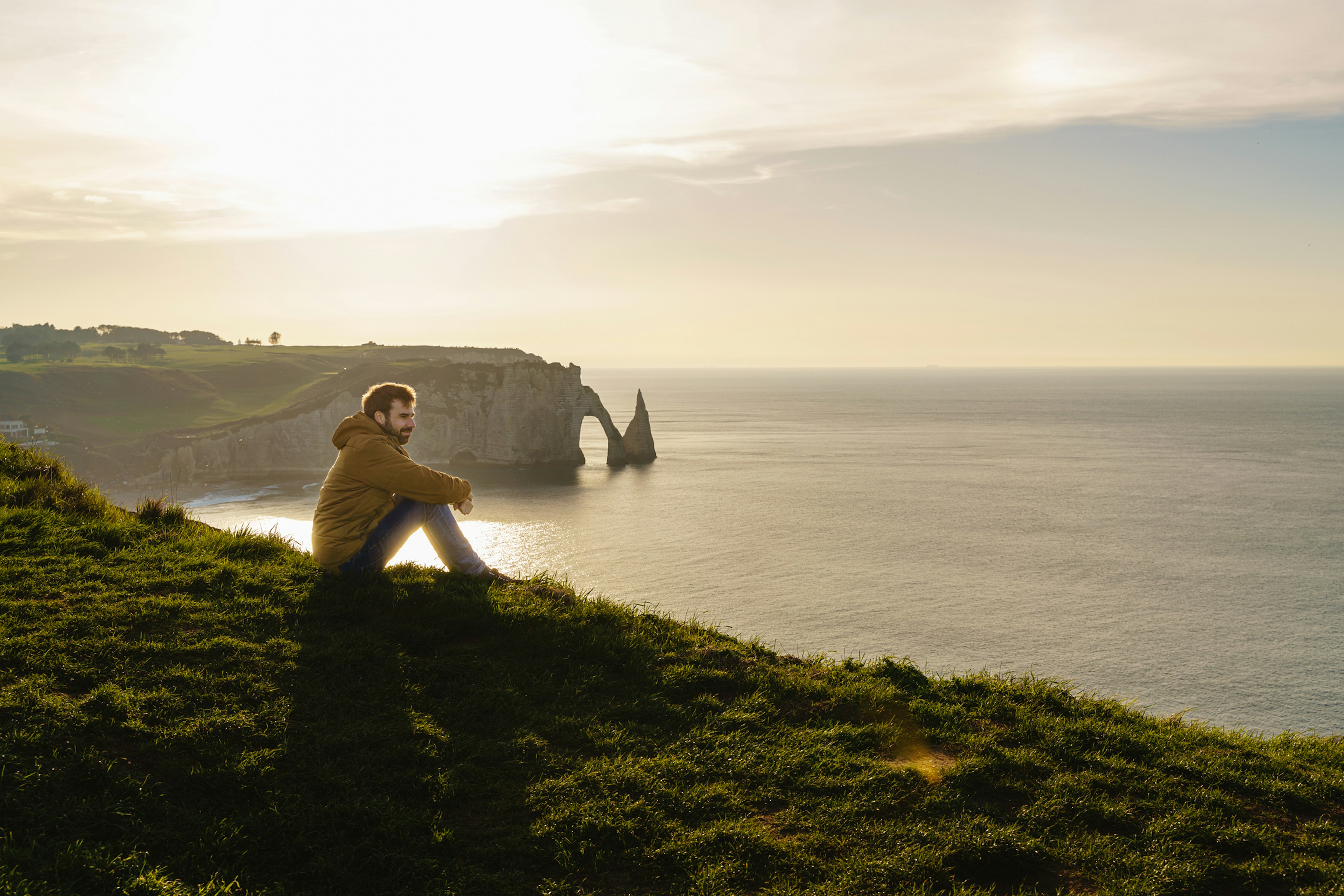 Horizontal panoramic view of caucasian man sightseeing at Etretat cliff at sunset.