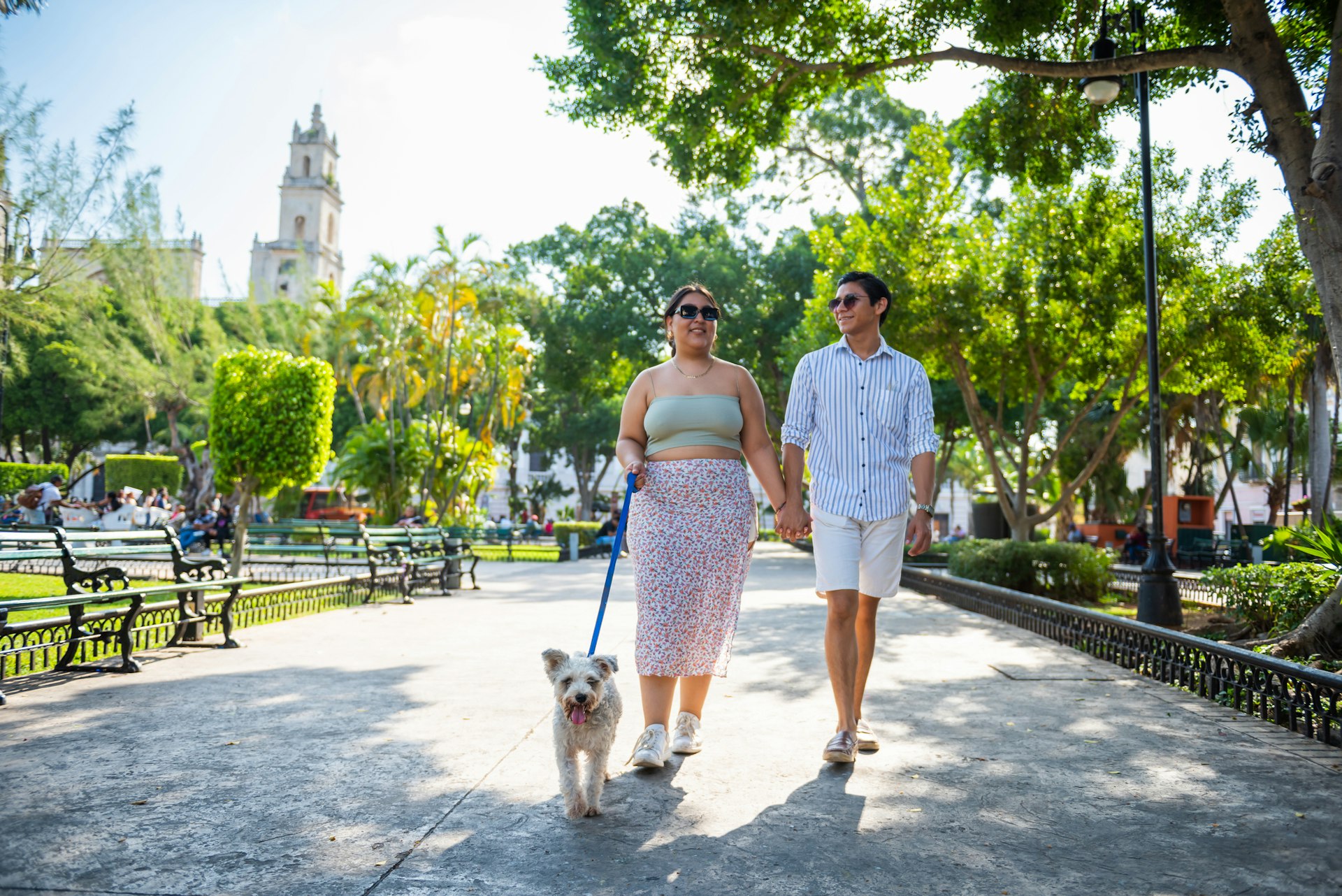 A young couple walk their dog near some colonial buildings in Merida, Mexico whilst holding hands