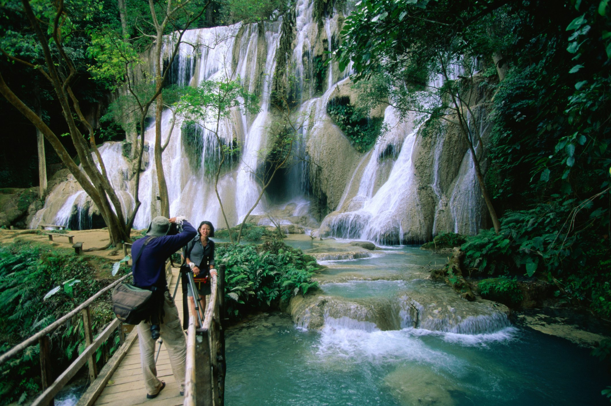 A man takes a photo of his wife in front of a waterfall with many separate cascades