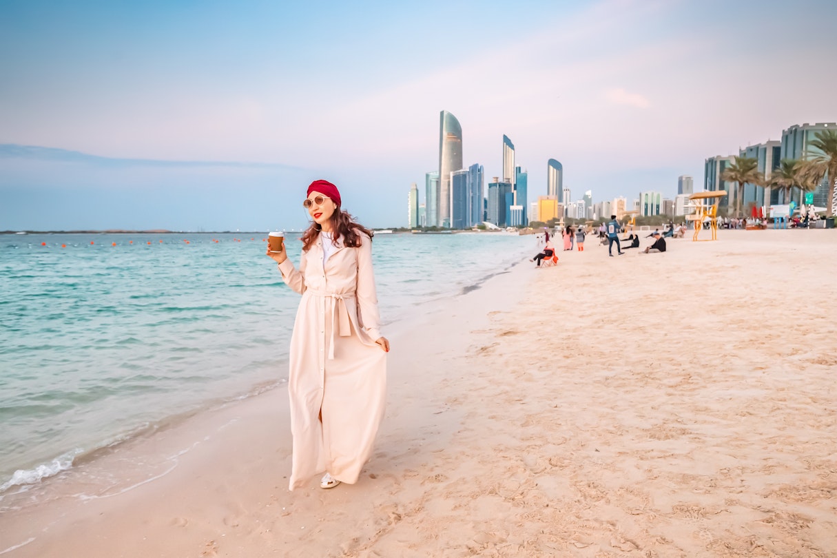 Happy girl walking on sandy beach with takeaway coffee with Abu Dhabi downtown skyscrapers in the background
1487684661