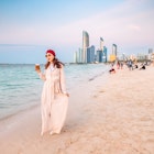 Happy girl walking on sandy beach with takeaway coffee with Abu Dhabi downtown skyscrapers in the background
1487684661