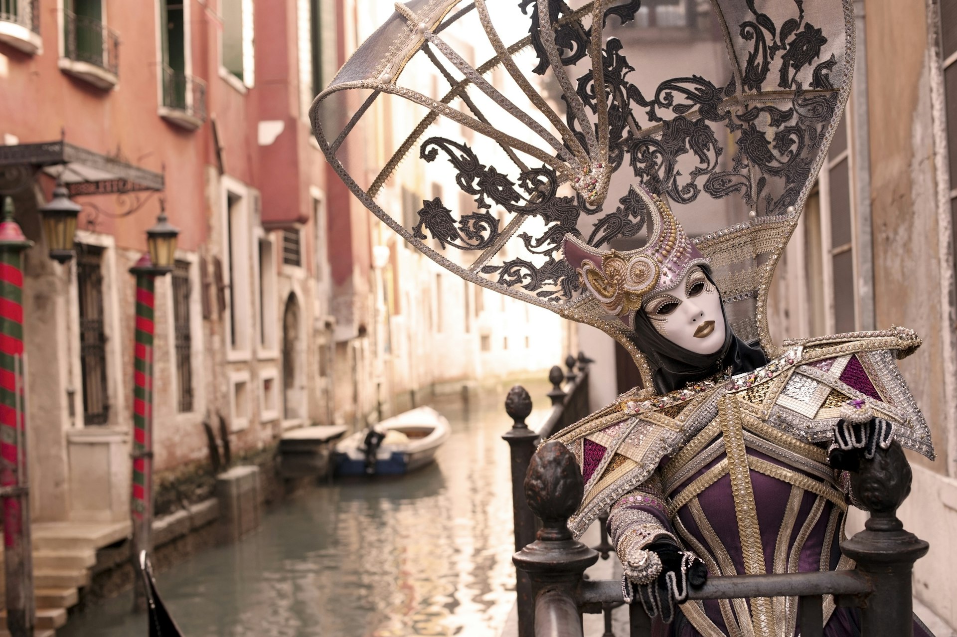 A masked person during the Venice Carnival. They are posing in front of house along one of the canals in Venice, Italy.
